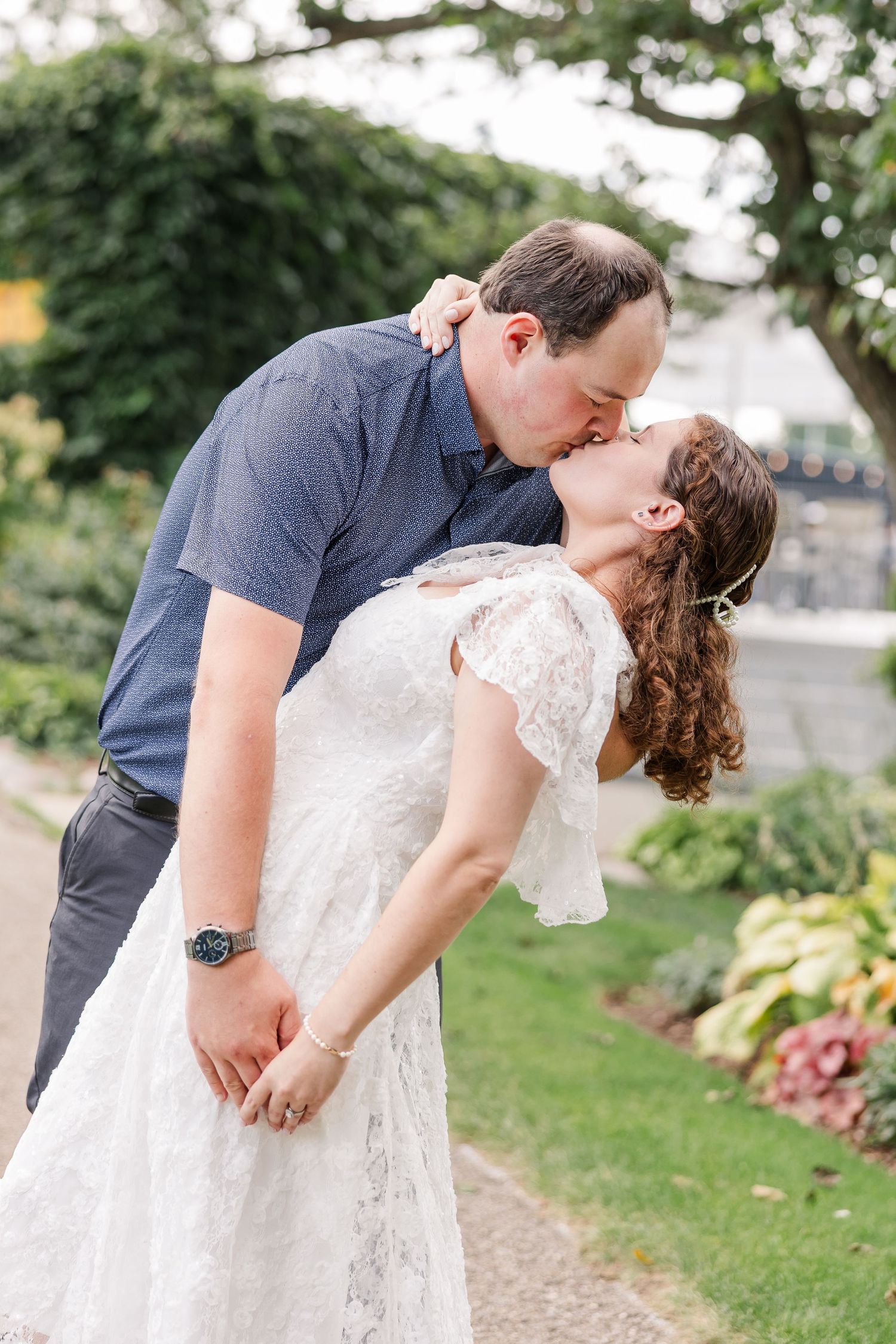 Couple sharing a romantic dip kiss outdoors in a garden, bride in lace wedding dress.