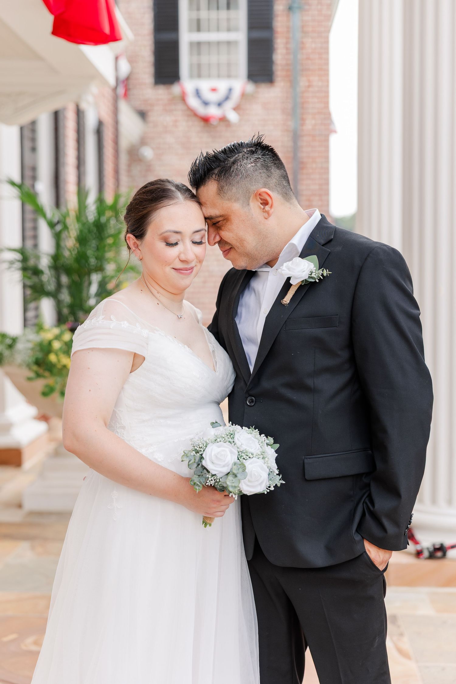 Bride and groom looking down together while holding her white and greenery wedding bouquet.