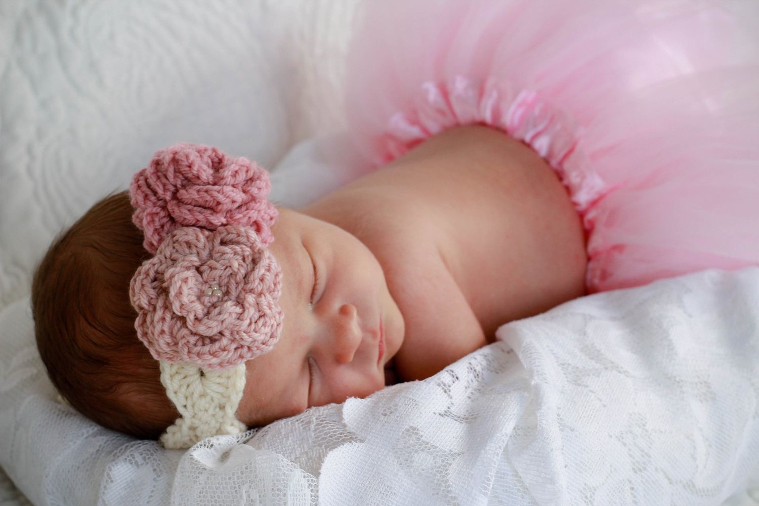 Baby sleeping on pink tulle fabric wearing a delicate floral headband.