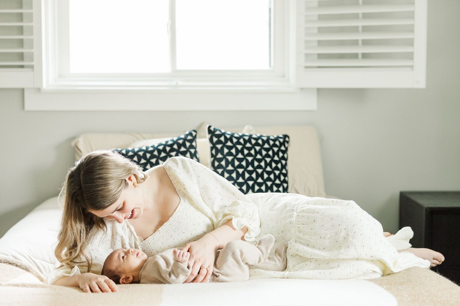 Mother lying on a bed smiling down at her newborn baby during an in-home lifestyle newborn photography session in Palatine Illinois
