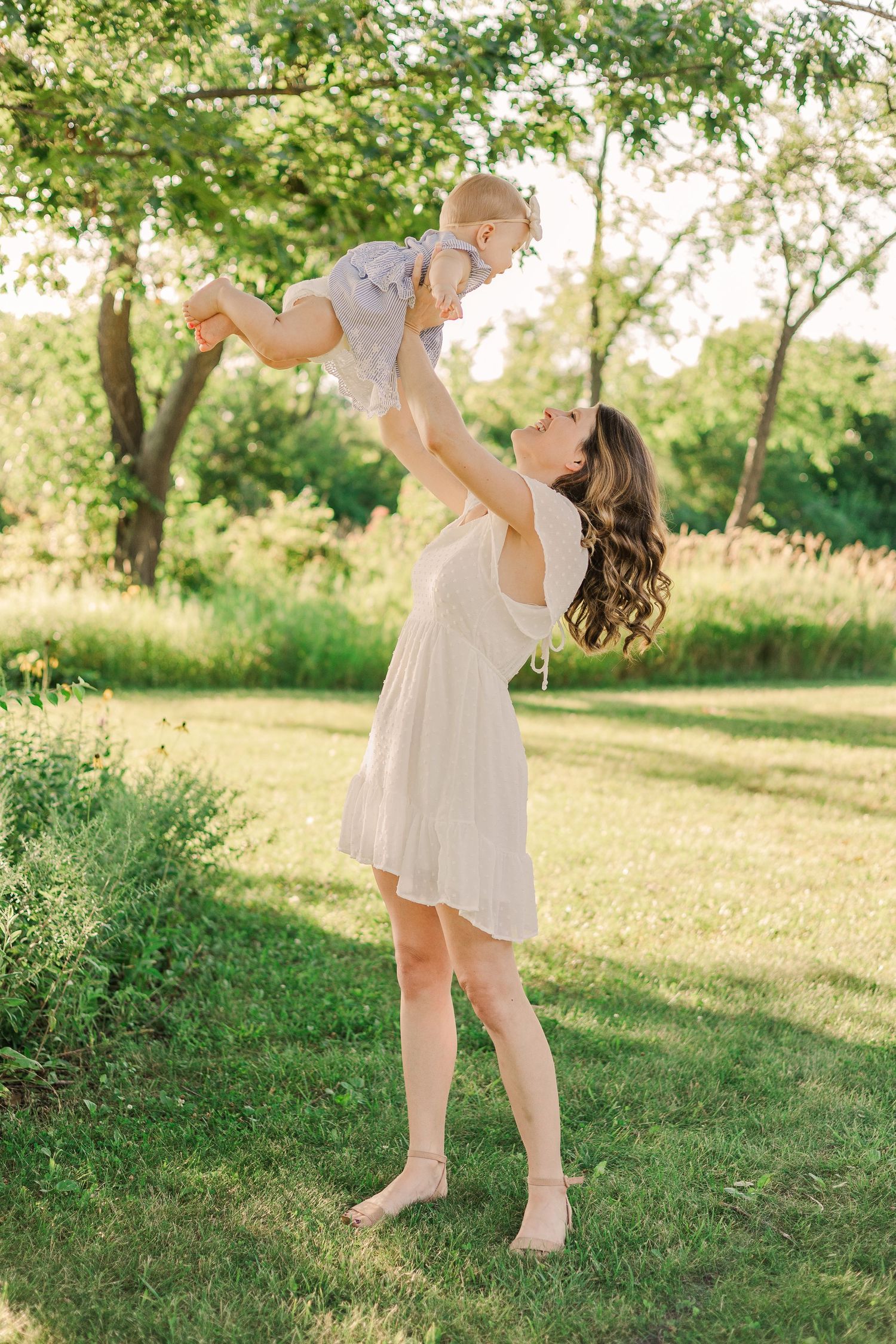 A parent lifts a small child playfully in the air in a sunlit garden setting.