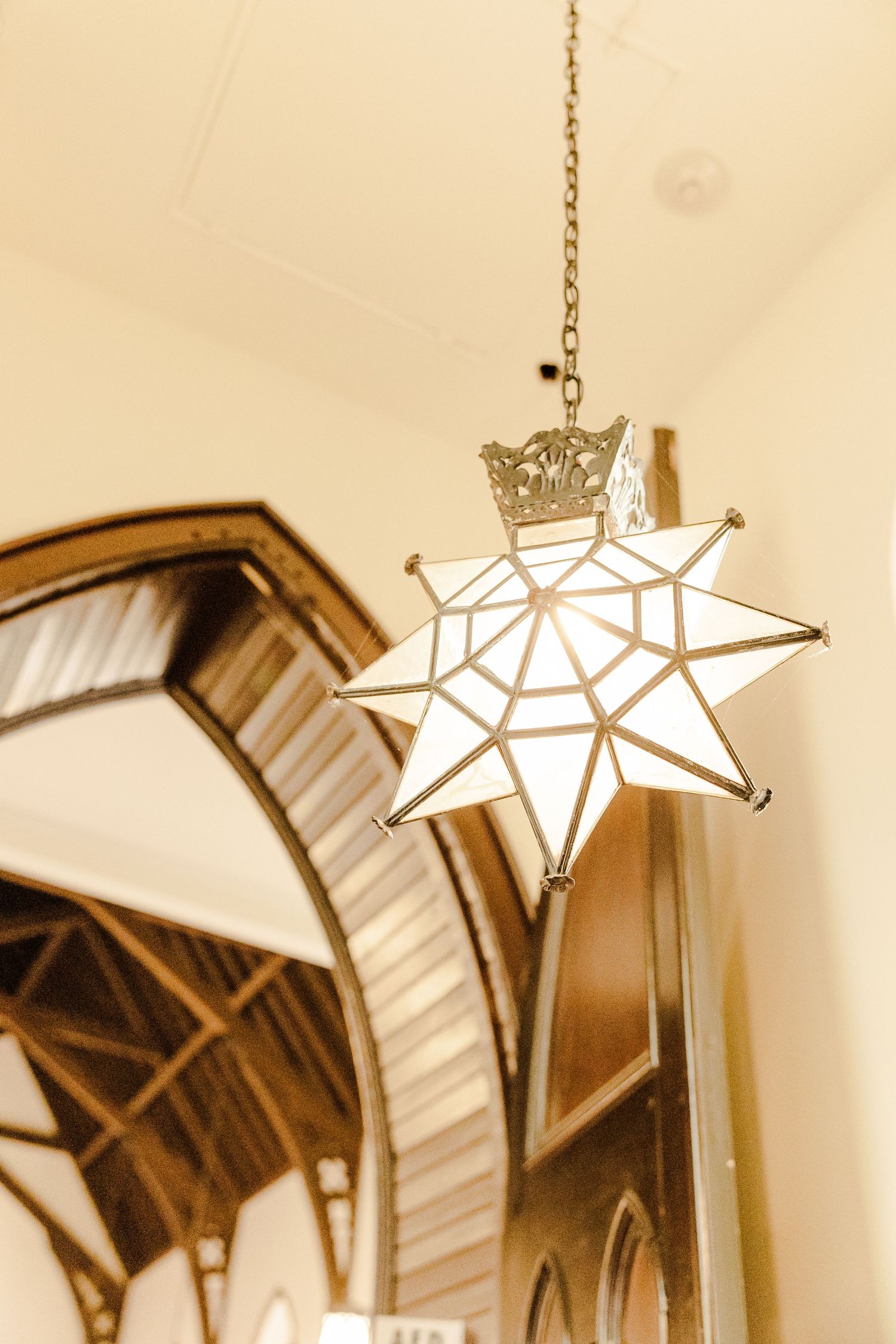 Decorative white star-shaped pendant light fixture hanging in a church with Gothic arched details.