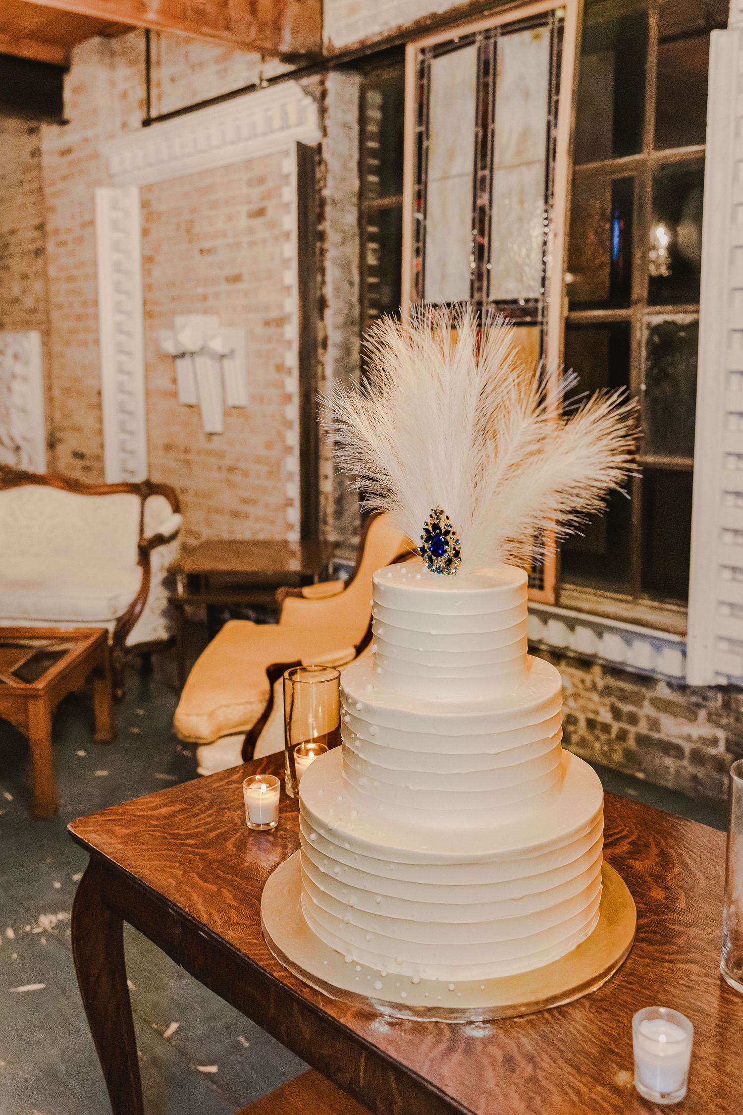An elegant white wedding cake decorated with feathers sits on a wooden table.