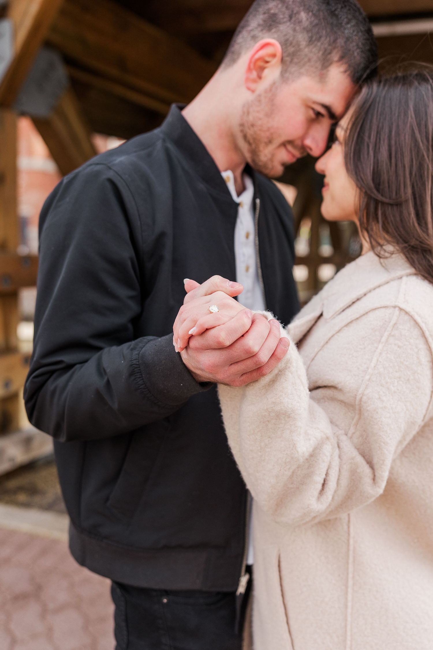 An intimate moment between a couple holding hands and leaning close under wooden rafters.
