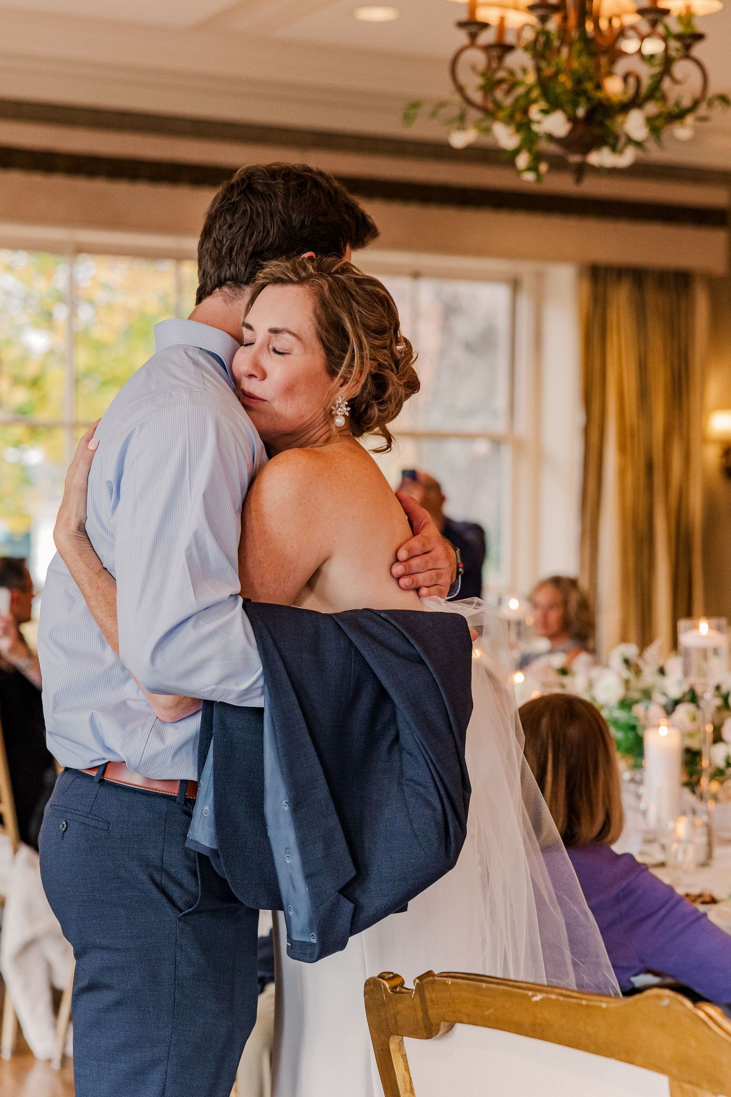 Couple sharing an intimate embrace during a wedding reception with elegant decor visible.