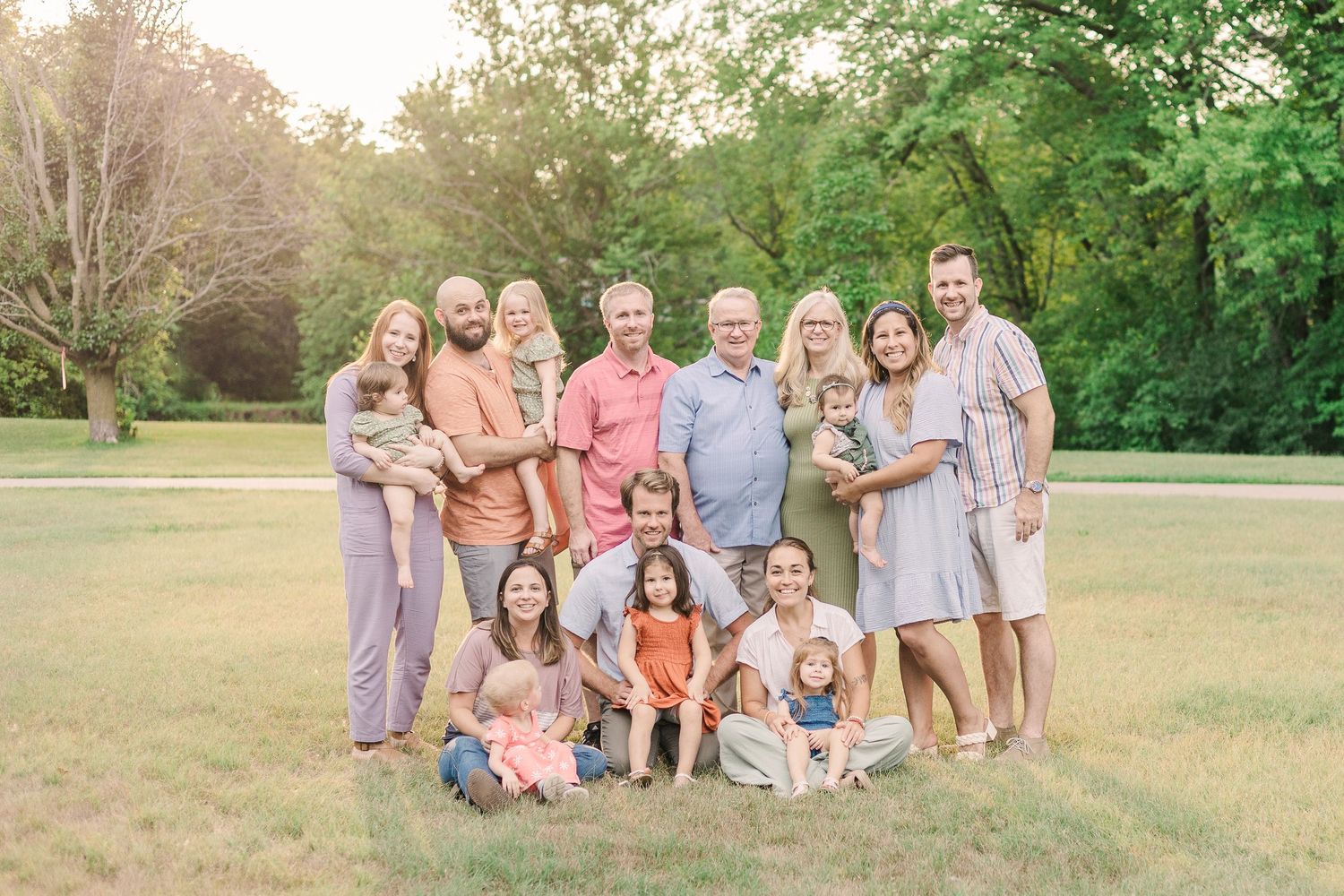 Large family group portrait taken outdoors in a park during golden hour.