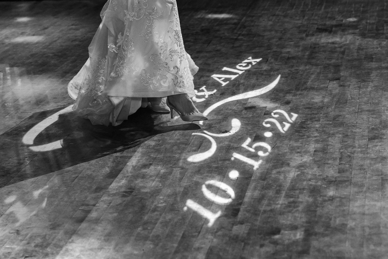 A wedding dress hem flows over text projected onto a dark dance floor.