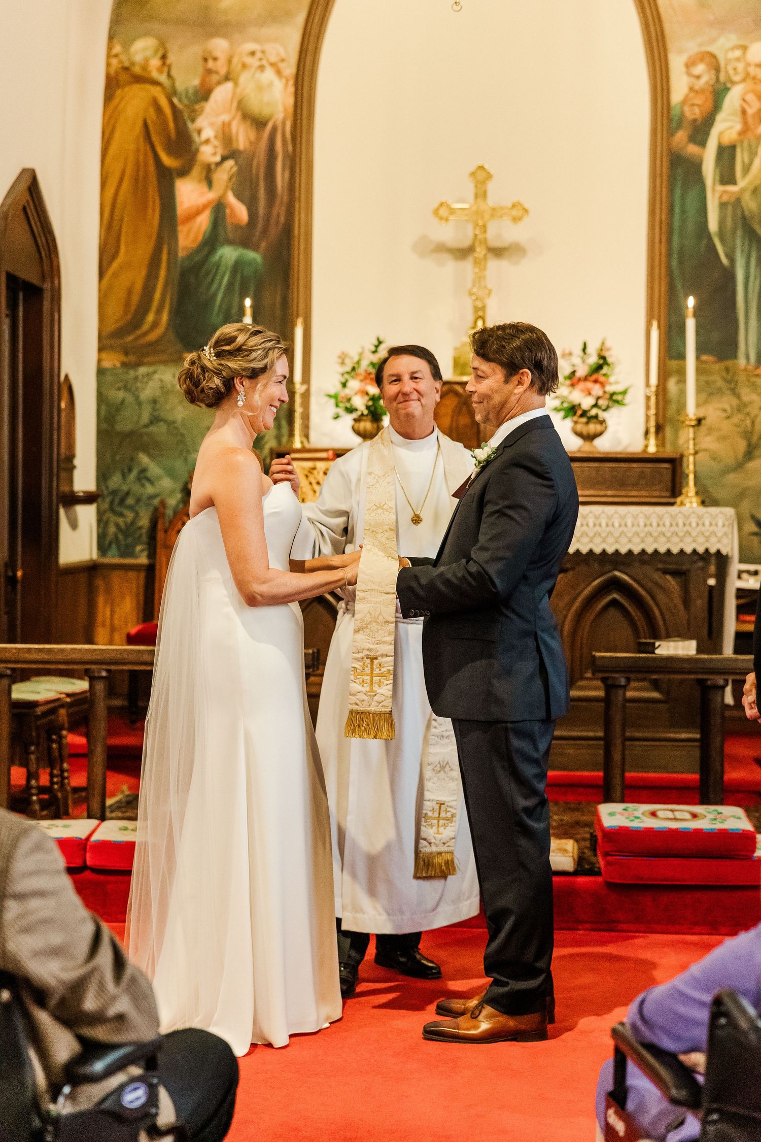 Traditional church wedding ceremony with priest officiating on red carpeted altar.