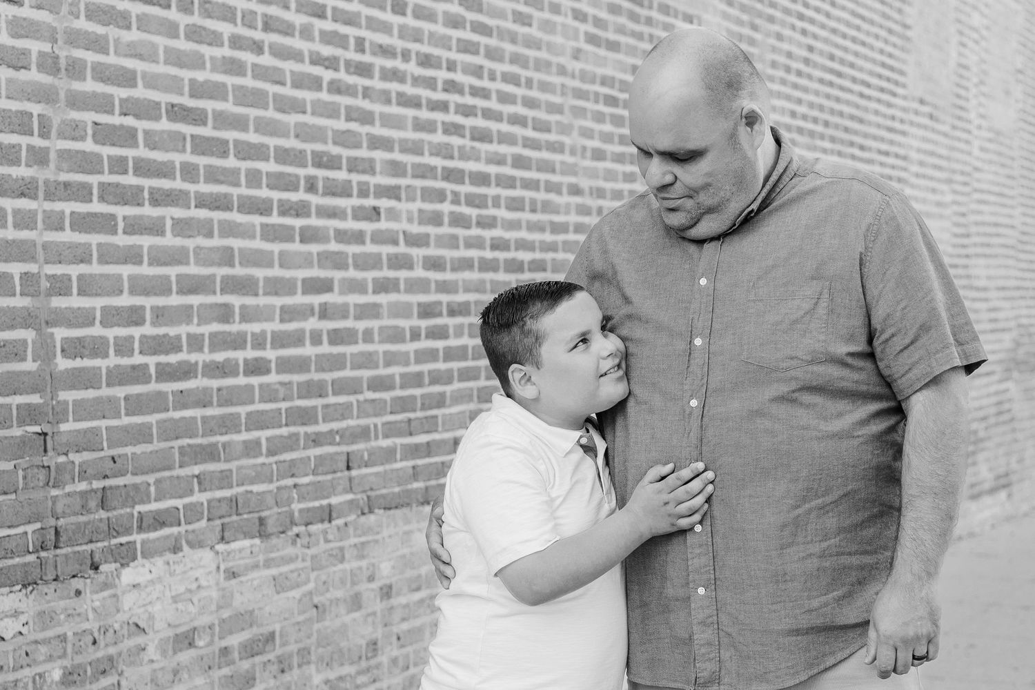 A tender black and white portrait of two people standing against a brick wall.