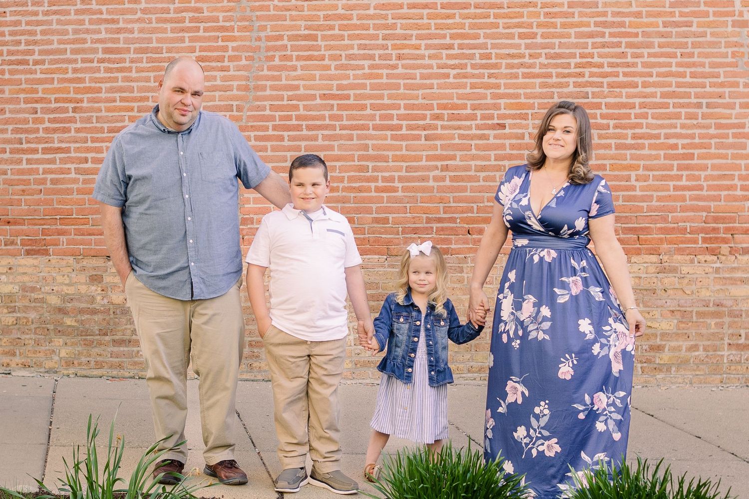 A family portrait taken outdoors with a red brick wall background and landscaping below.