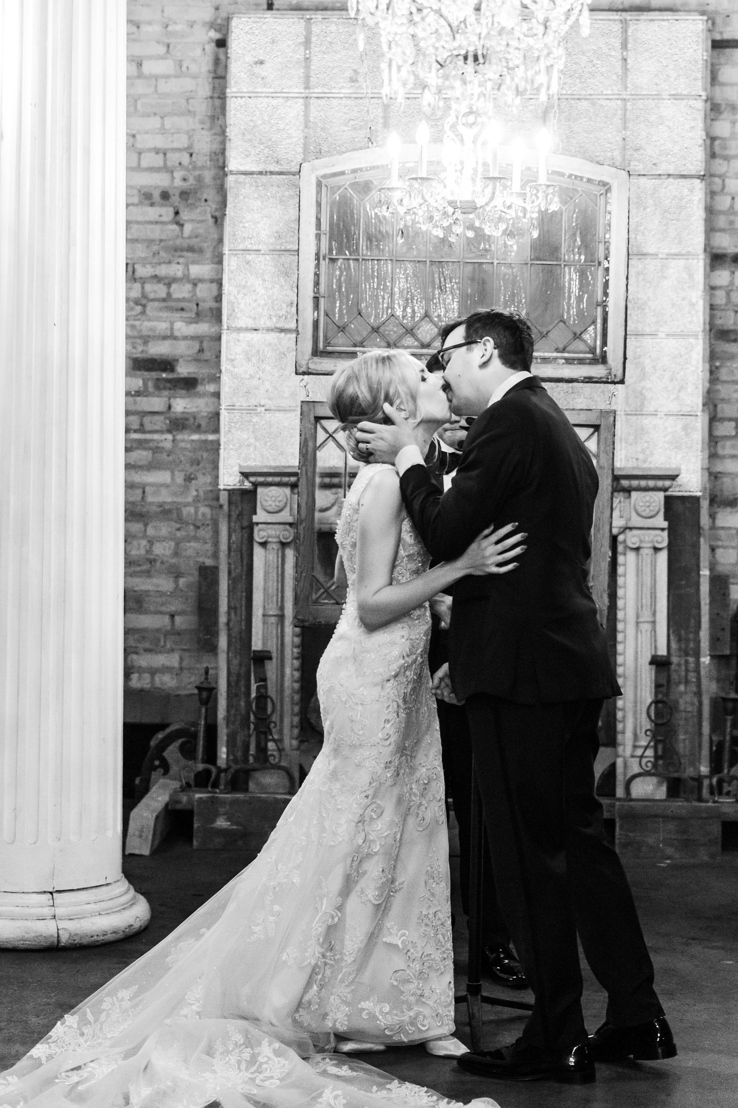 Black and white photo of a wedding couple kissing beneath a crystal chandelier.