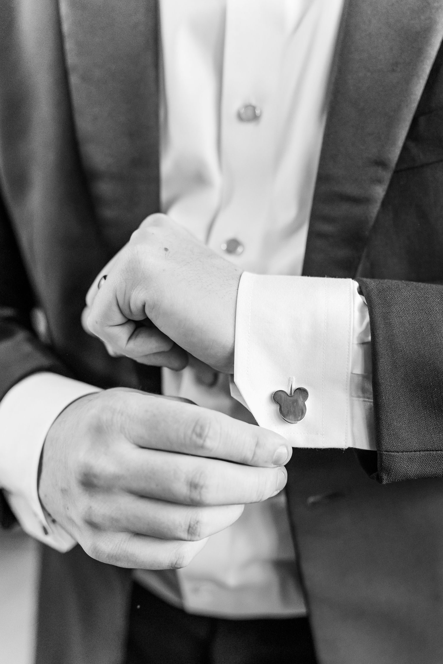 Black and white detail shot of hands adjusting Mickey Mouse cufflinks on formal attire.