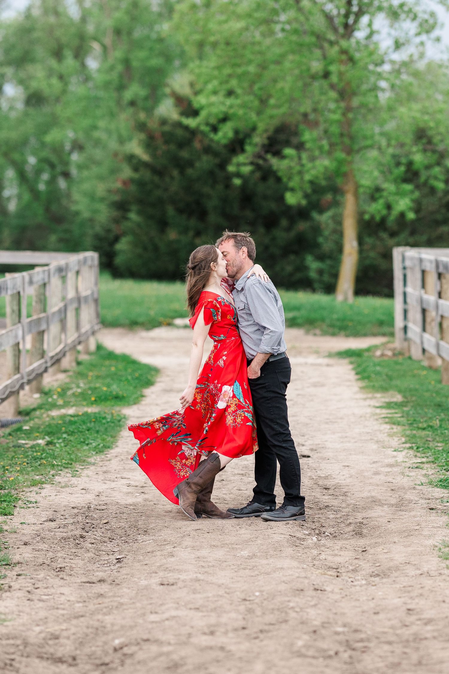Romantic moment captured on a rustic dirt path between wooden fences.