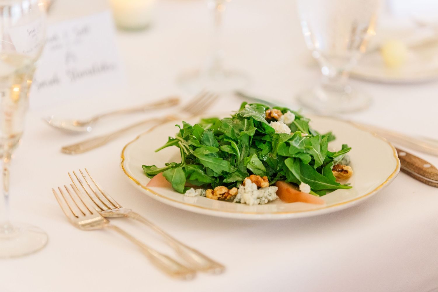 Fresh green salad plated elegantly on white china with gold trim and formal place settings.