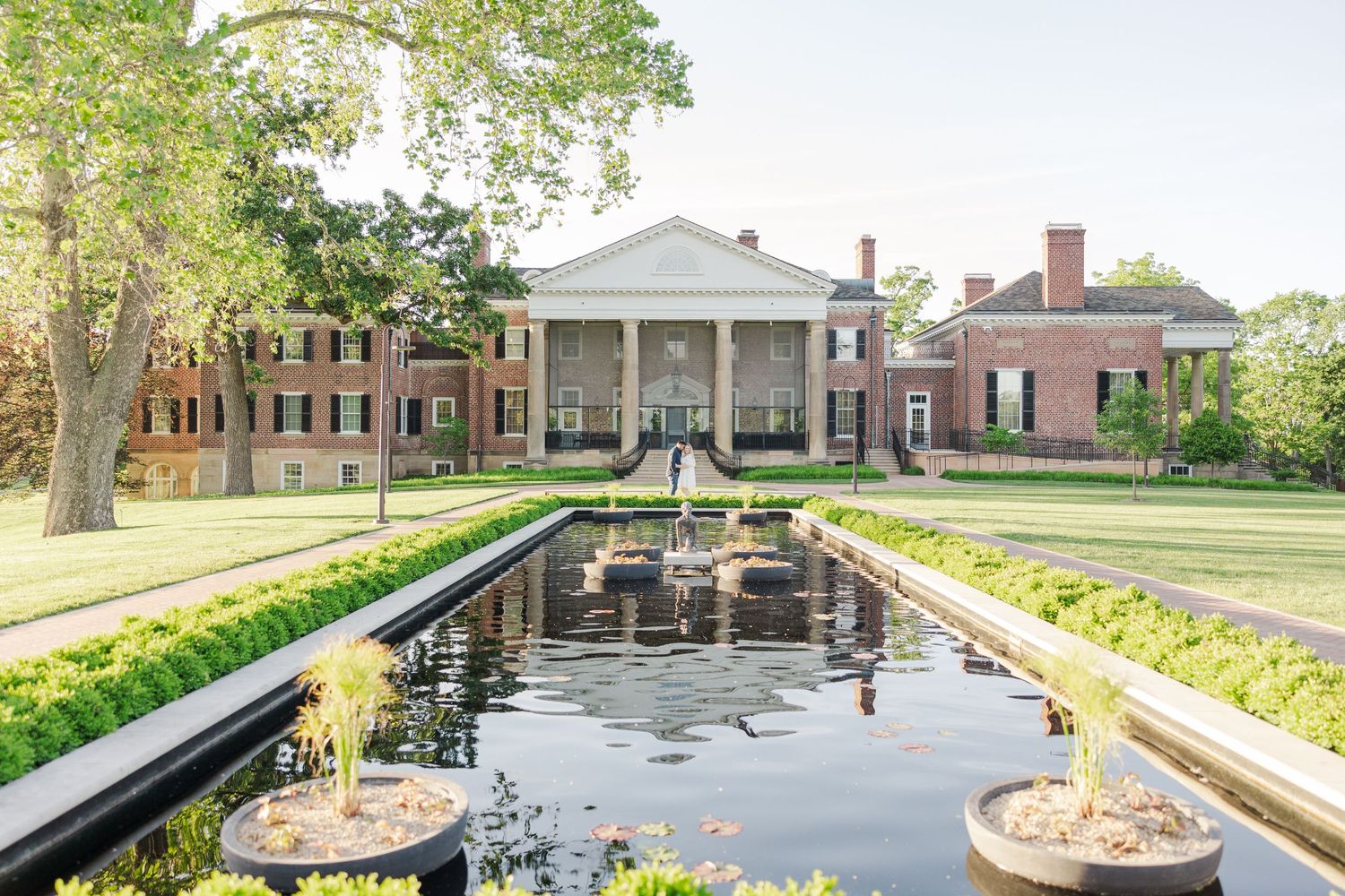 Stately colonial mansion with symmetrical architecture and reflecting pool lined with manicured gardens.