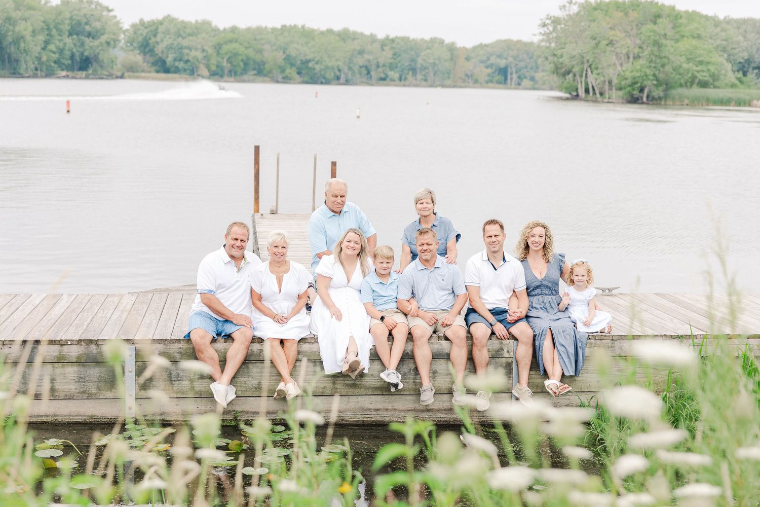 Multiple generations of a family gathered on a wooden dock by a peaceful lake.
