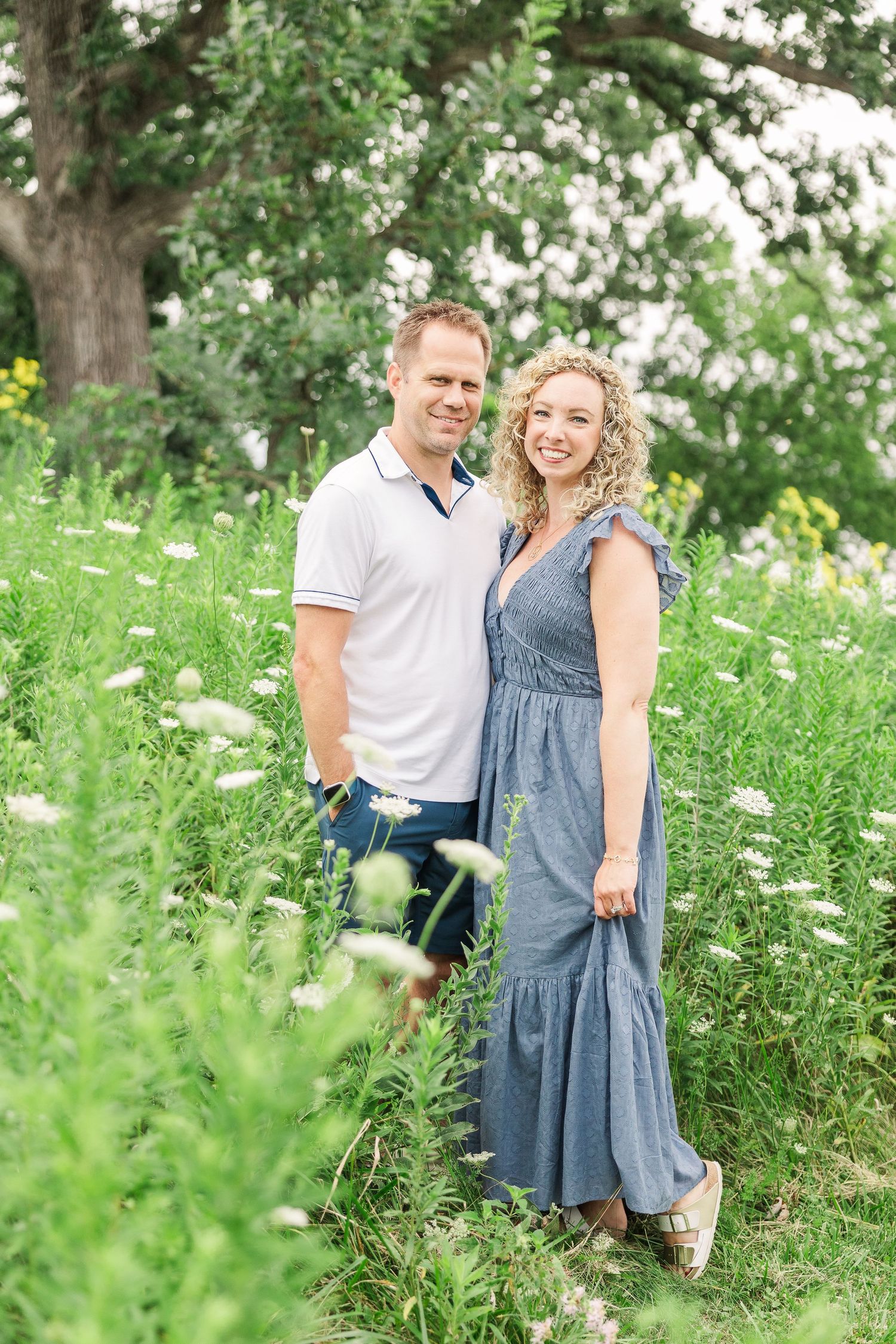 A summer portrait of a couple in coordinating outfits standing among wildflowers.
