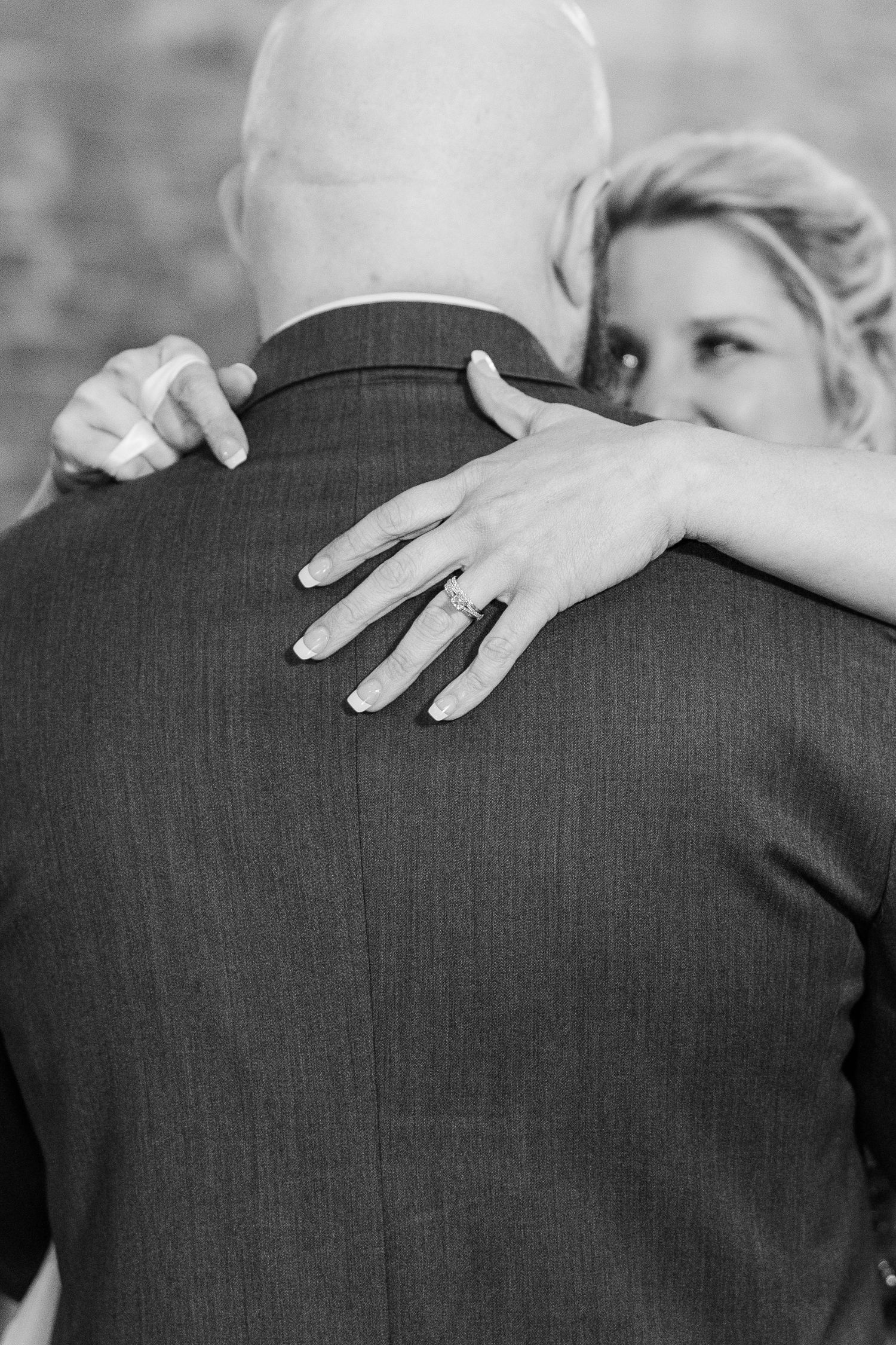 Close-up black and white photo showing a bride's hands with wedding ring embracing during a dance.