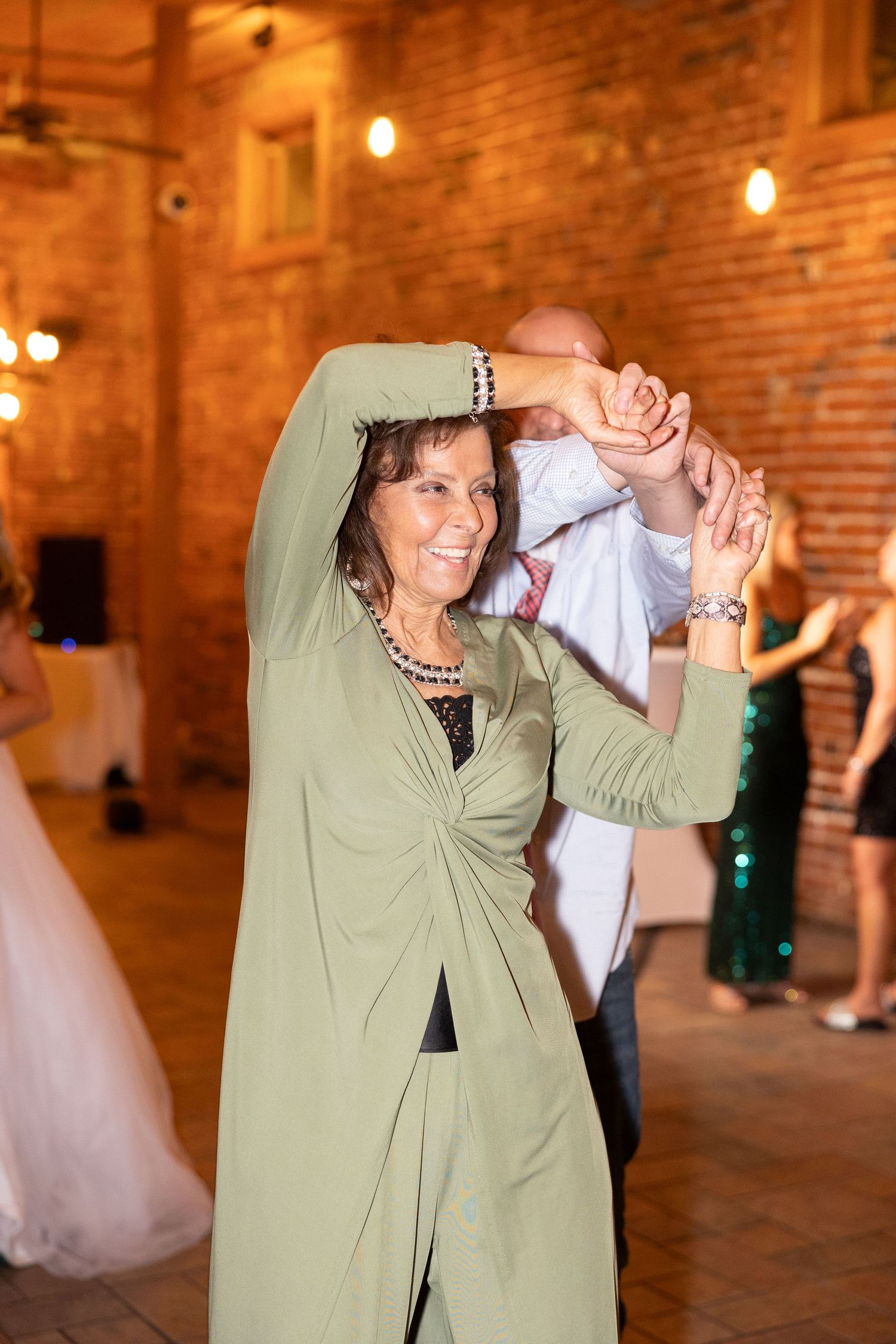 Guest dancing joyfully at wedding reception in sage green outfit.