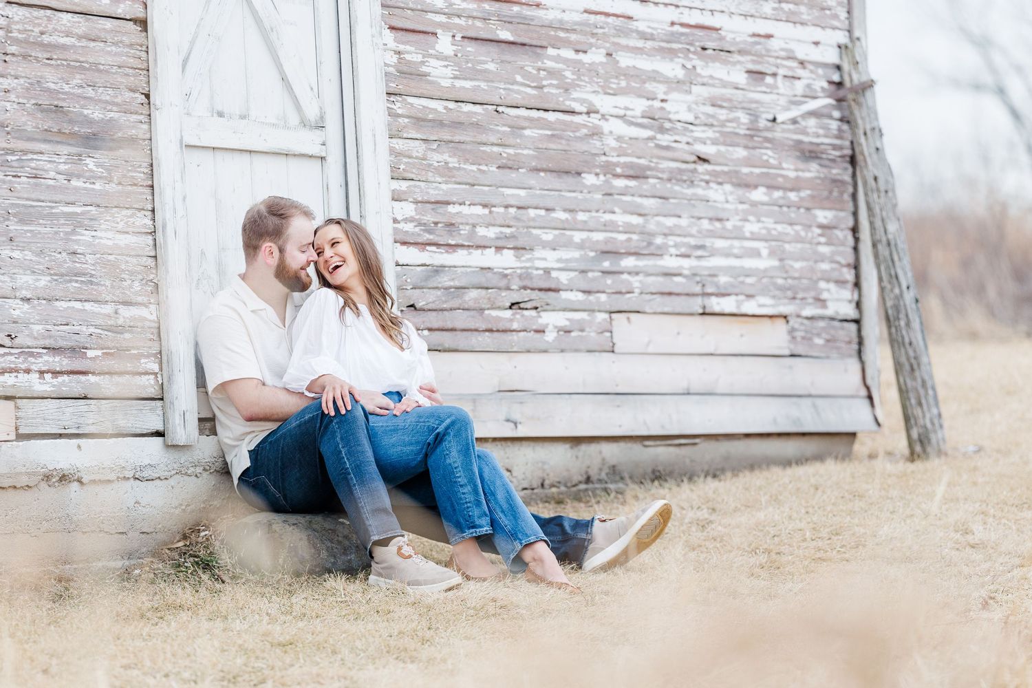 Couple sitting by rustic barn during pregnancy announcement photos in Cary, Illinois
