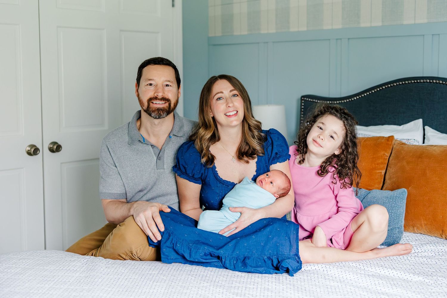 Family of four sitting on bed during bright in-home lifestyle newborn session in Crystal Lake, Illinois