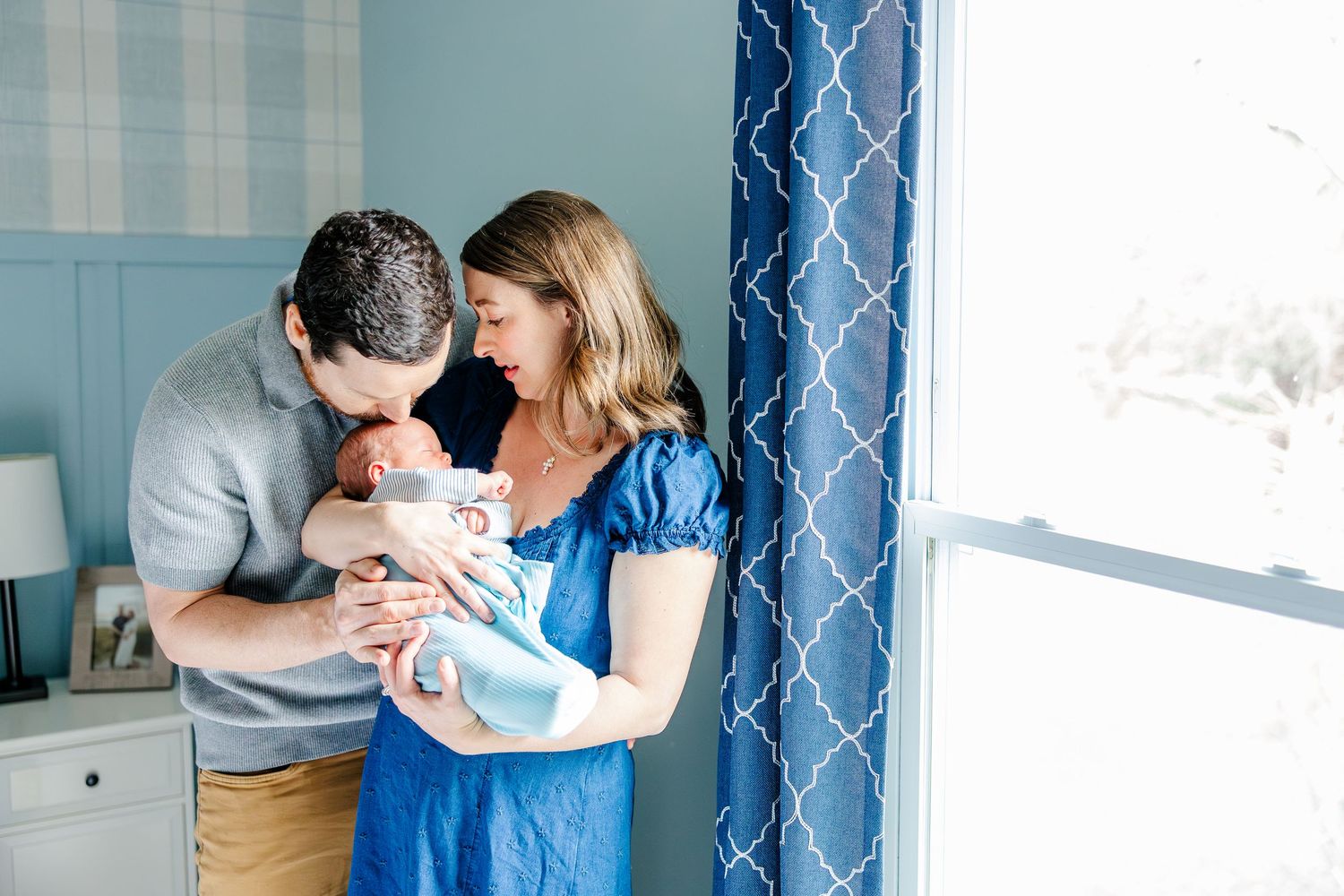 Parents snuggling newborn son by window during in-home lifestyle newborn session in Crystal Lake, Illinois