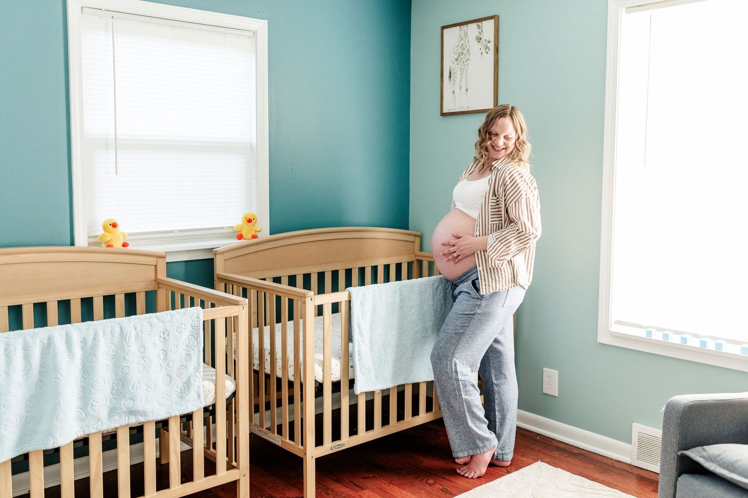 Mother standing beside twin cribs in the nursery during an in-home maternity session in Crystal Lake.