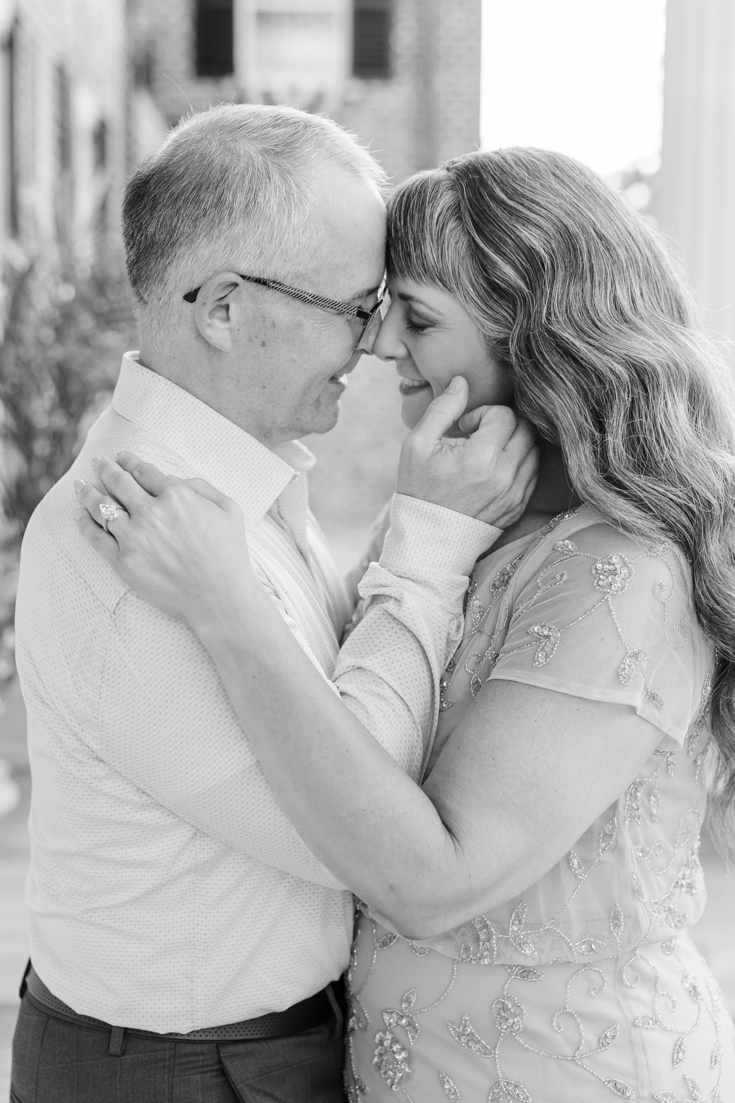 Black and white photo of a couple sharing a tender romantic moment, touching foreheads and smiling outdoors.