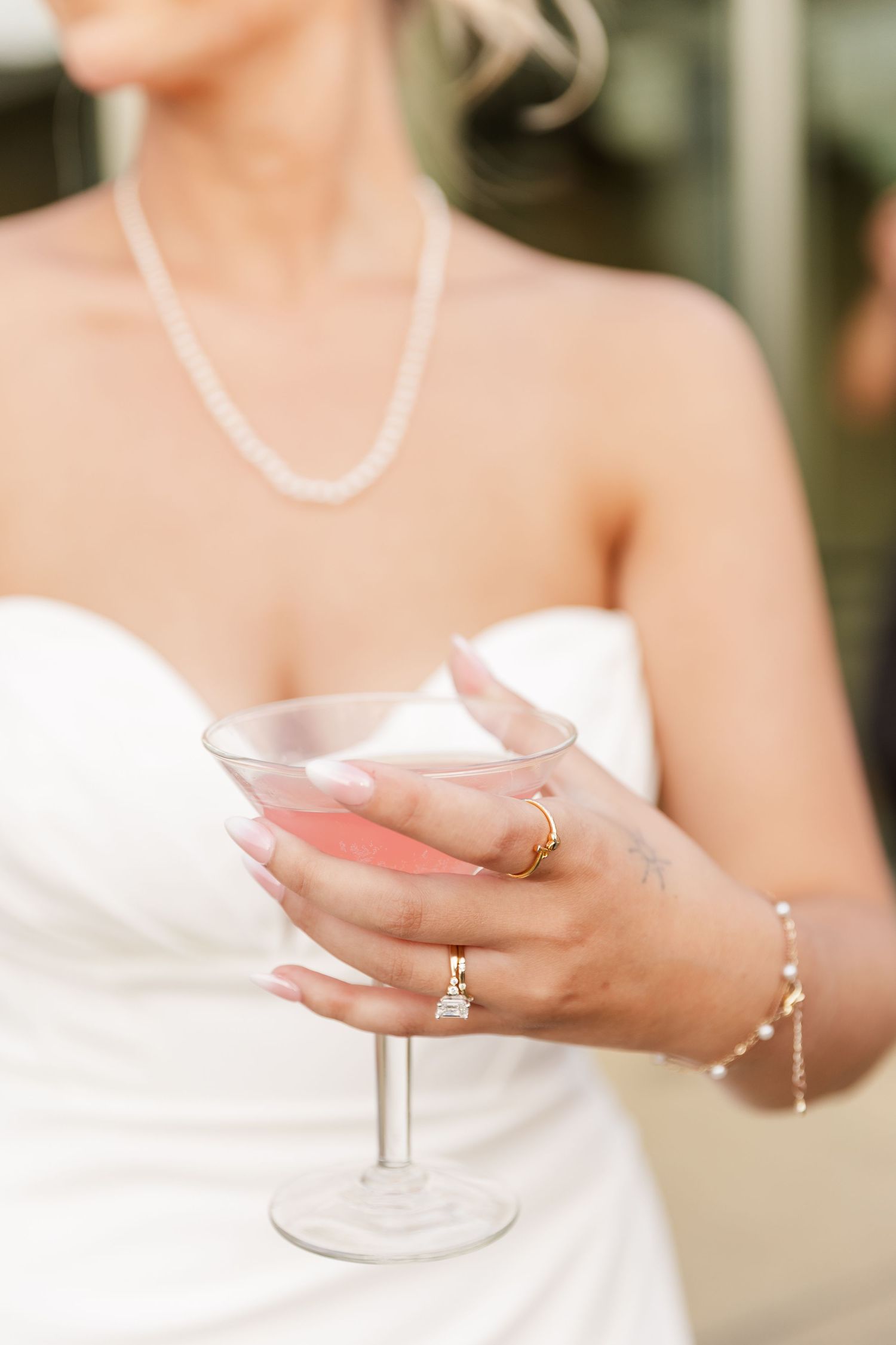 Bride in white strapless gown holding a pink cocktail drink with diamond engagement ring.