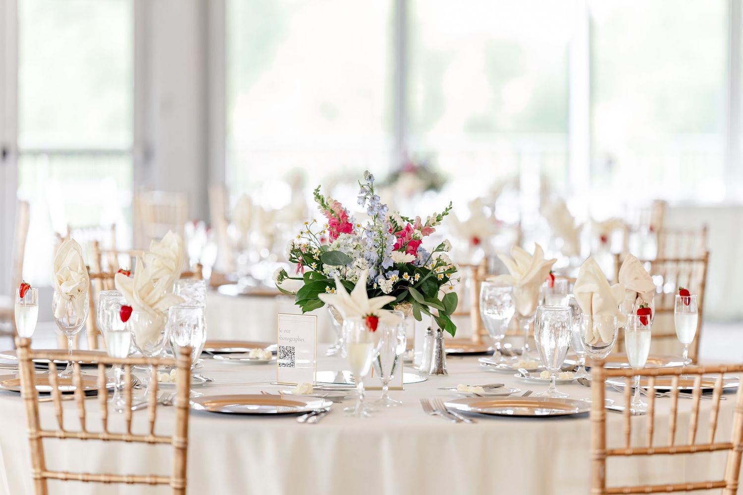 Elegant wedding reception table set with gold chiavari chairs, floral centerpieces, and crystal glassware.