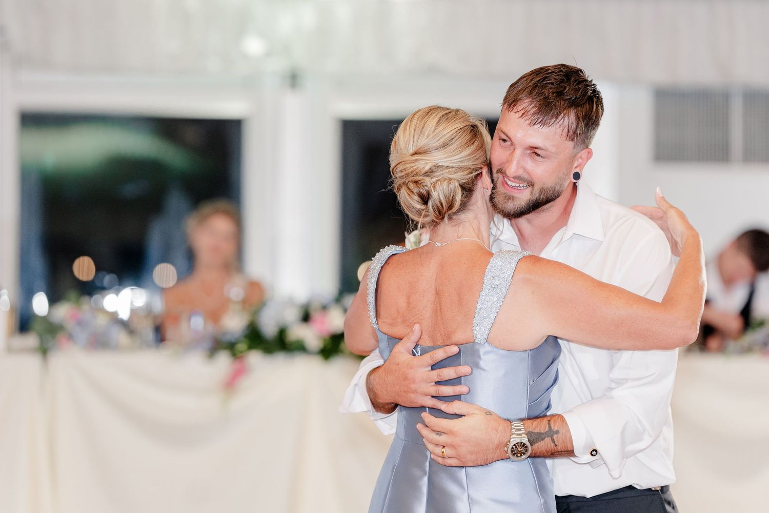 Groom embracing a woman in a blue dress during a dance at wedding reception.