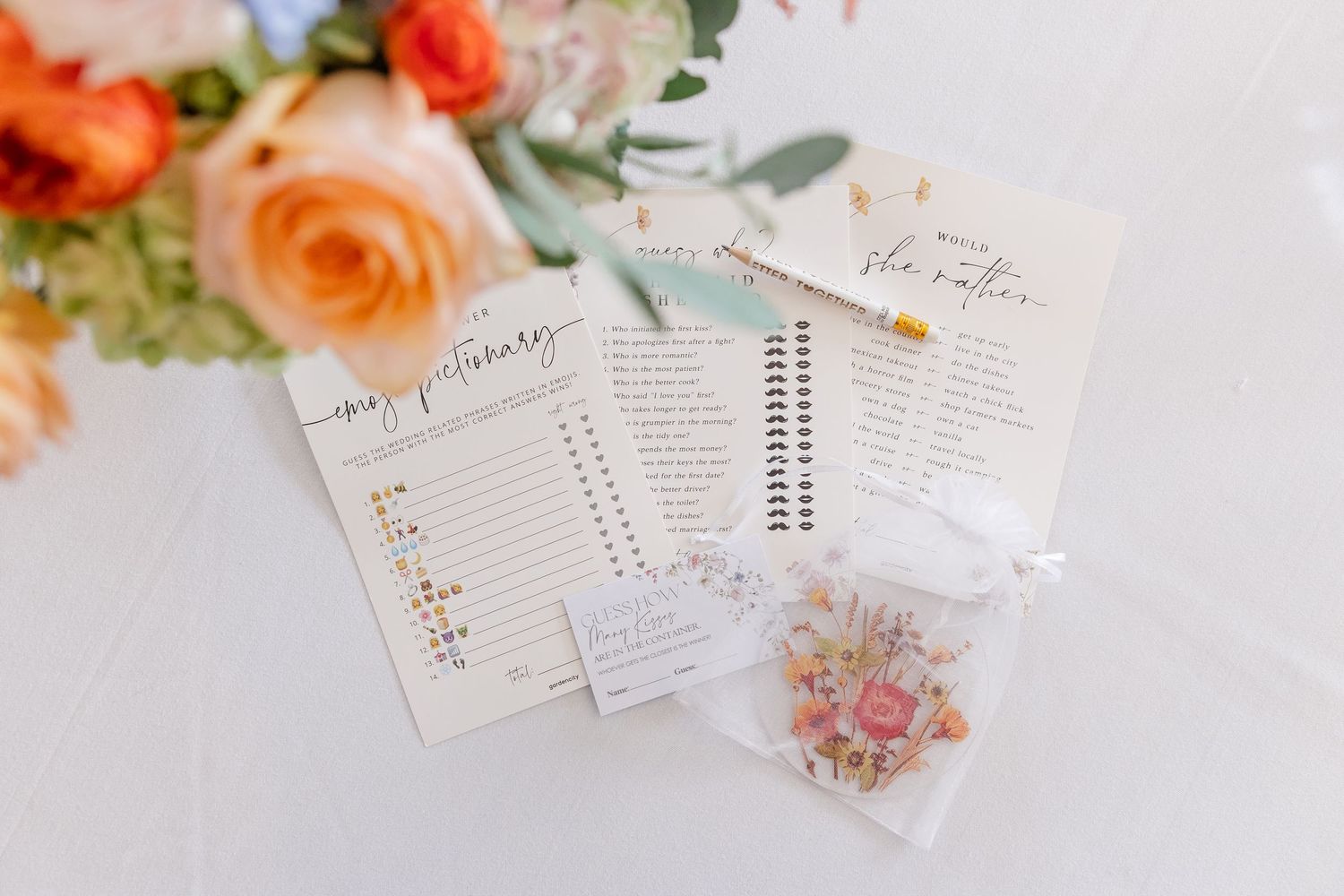 Bridal shower game cards and floral favor bags arranged on a white table with peach and orange flowers.