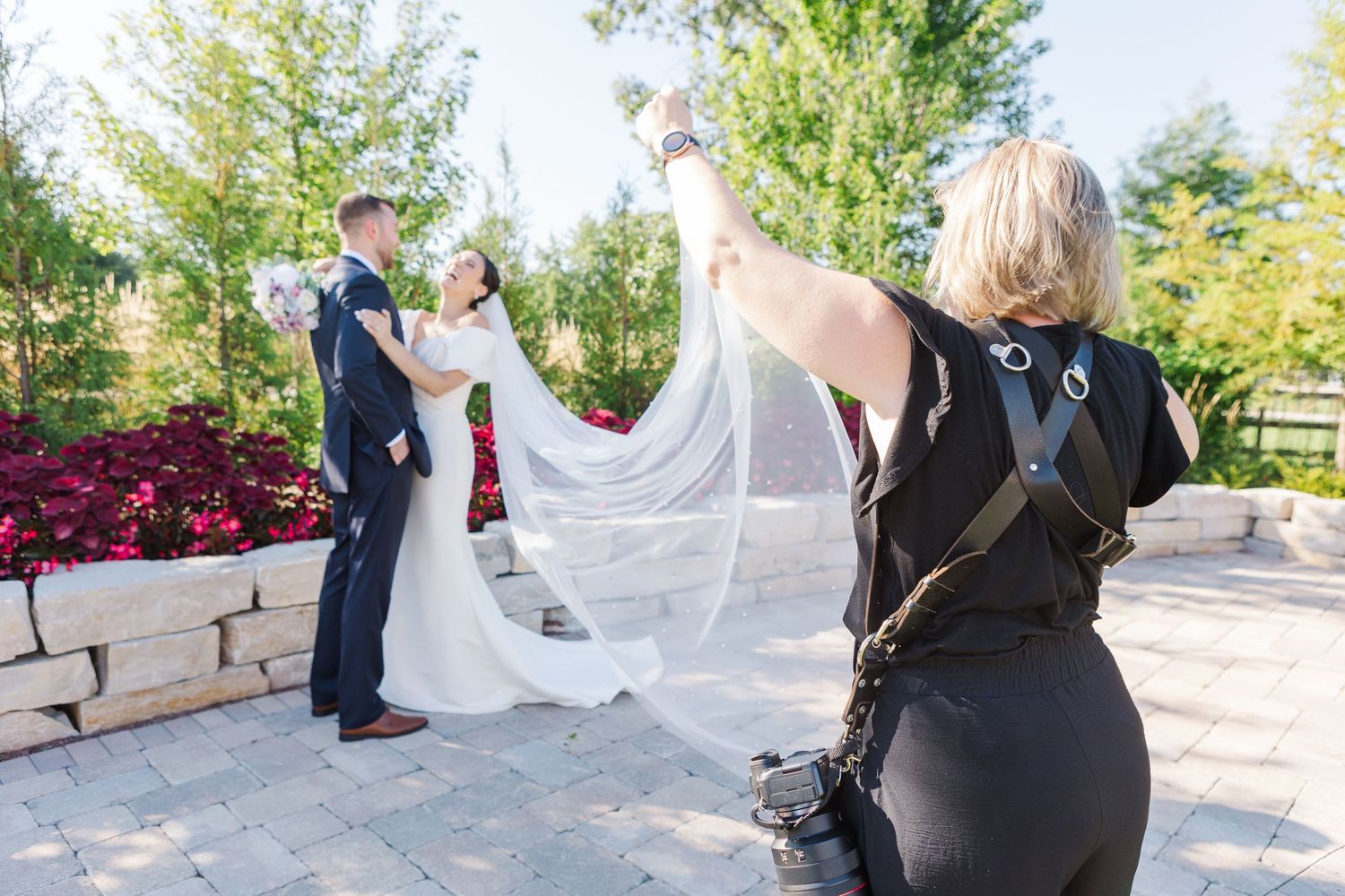 Cassie Lacina lifting a bride’s veil while photographing outdoor wedding portraits