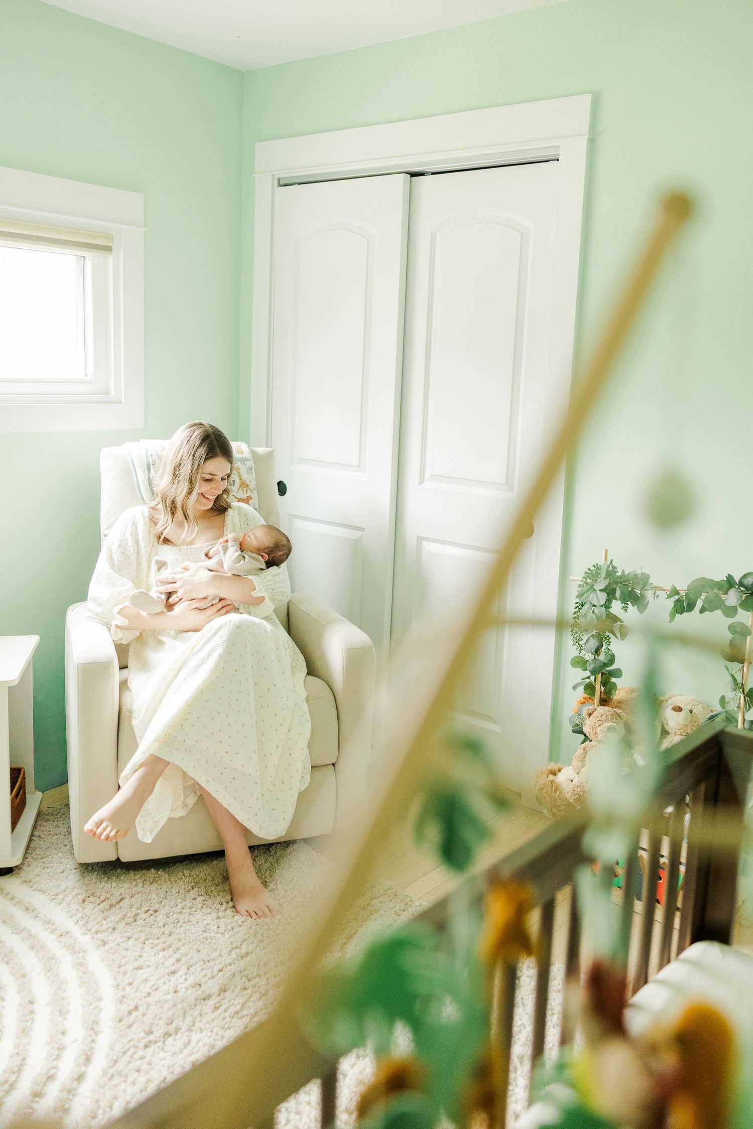 Mother holding her newborn baby in nursery chair during an in-home lifestyle newborn session in Palatine Illinois