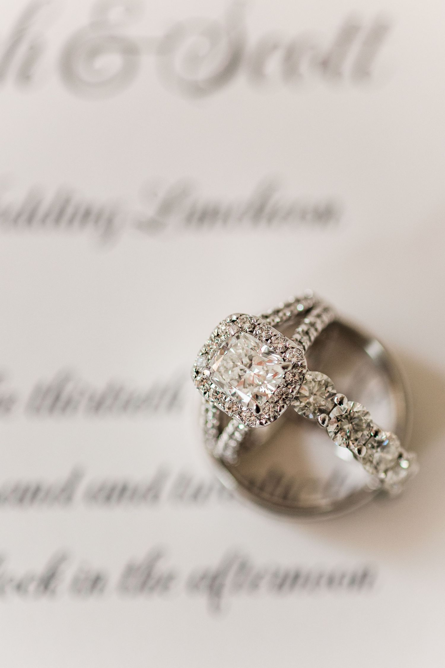 Close-up of diamond engagement ring with halo setting on wedding invitation text.