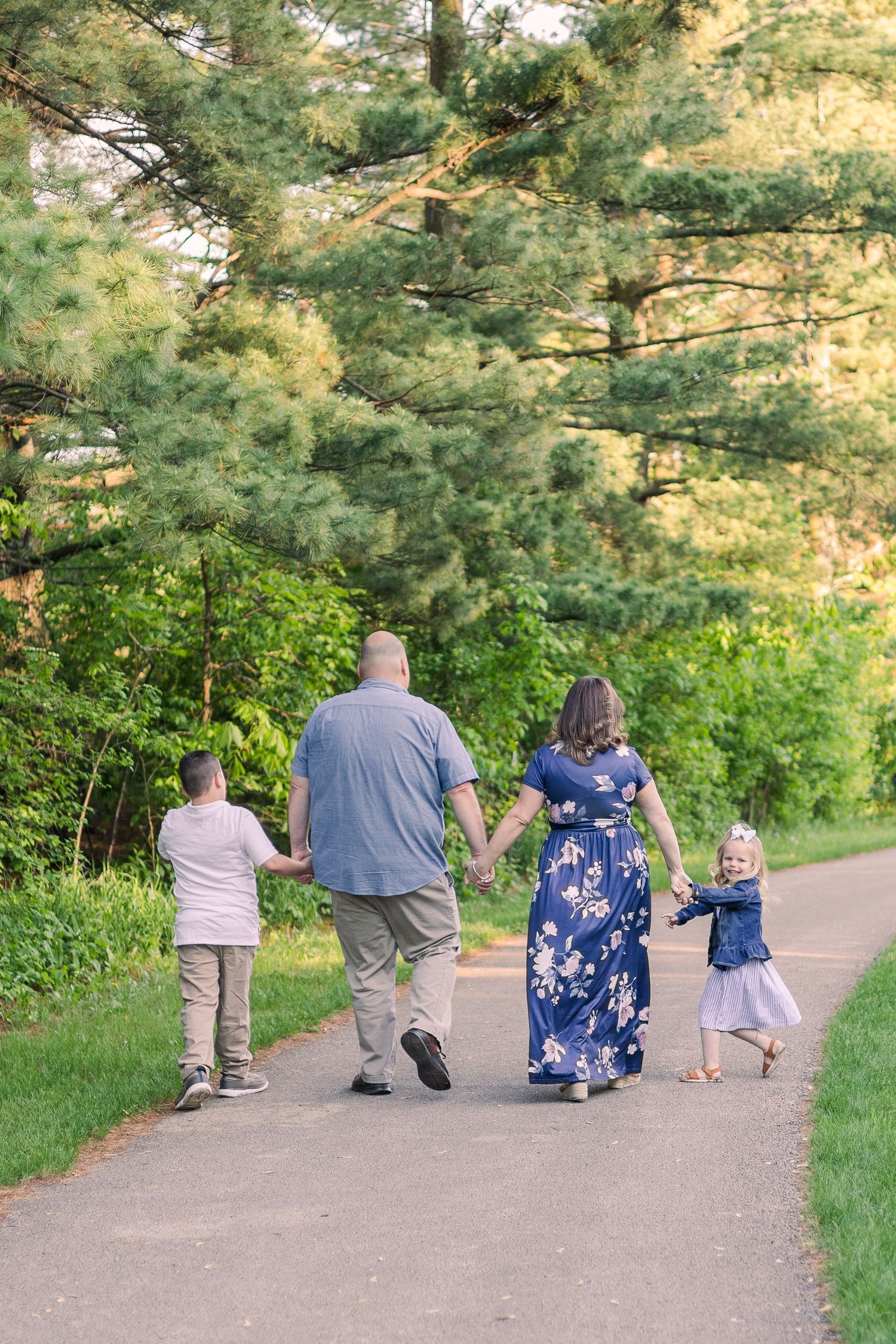 Family walking together on a scenic path surrounded by tall pine trees and lush greenery.