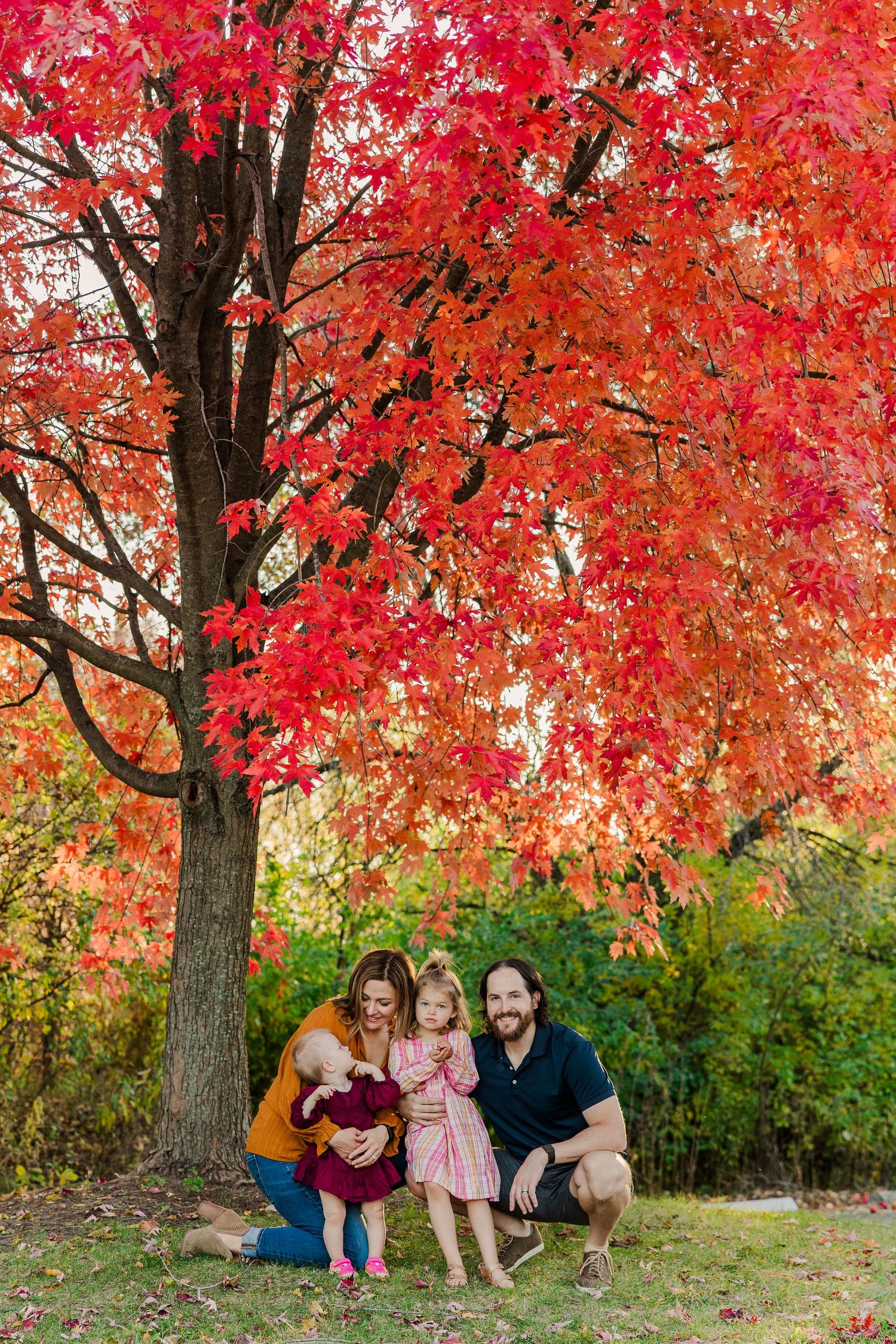 A family group poses beneath a vibrant red maple tree in fall.