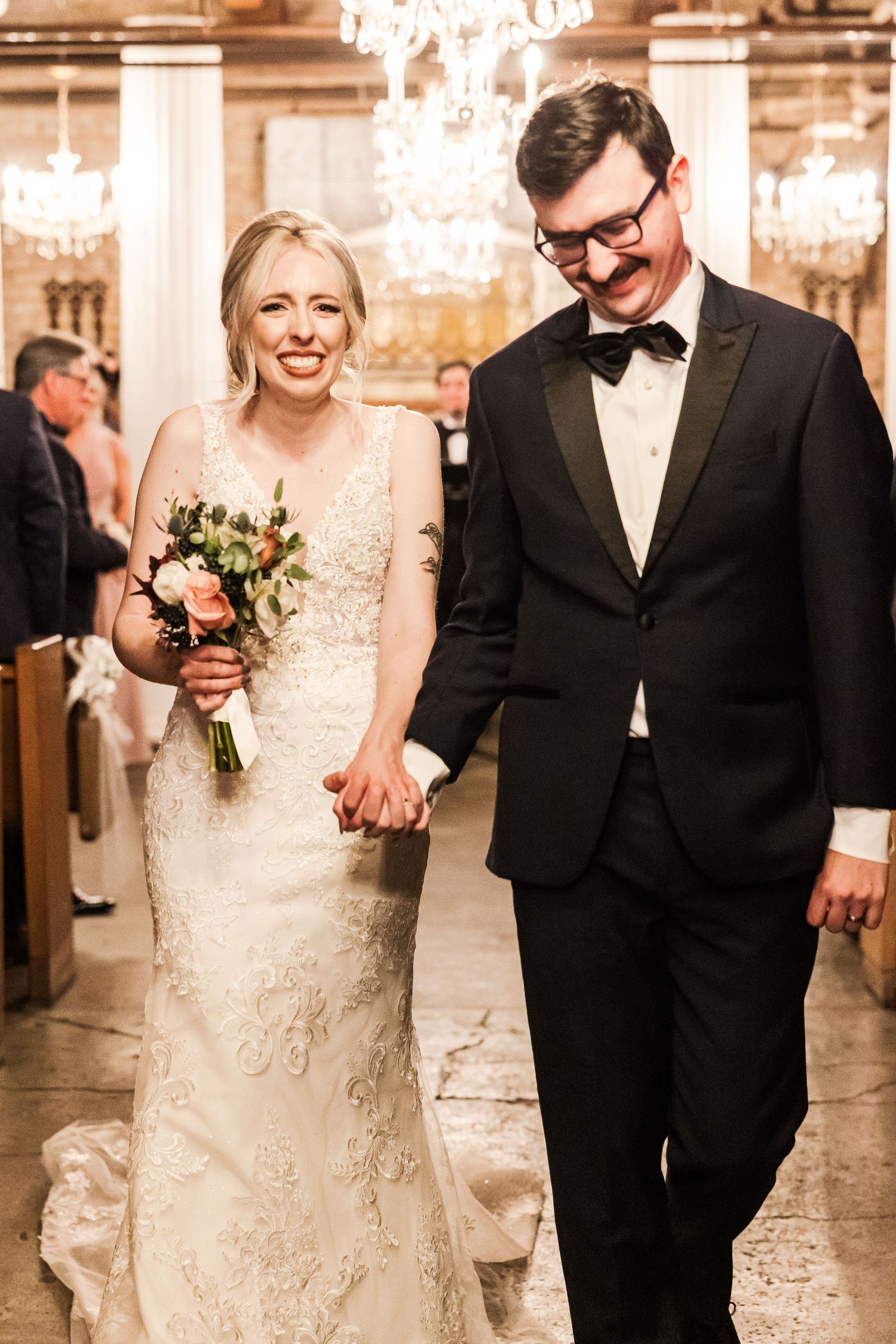 Newlyweds walk together holding hands while sharing joyful smiles in an elegant venue.