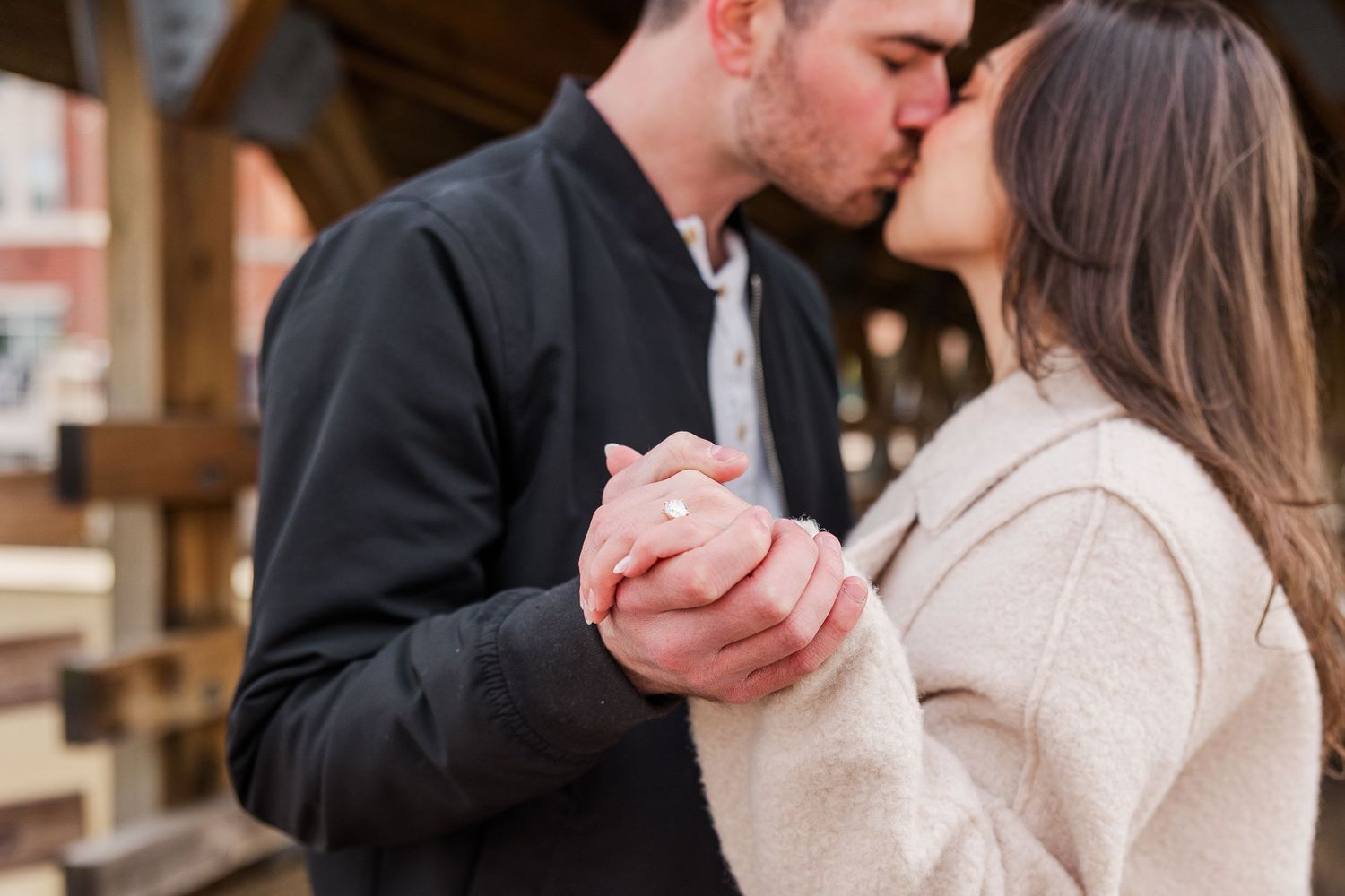 A romantic moment captured as a couple holds hands and leans in close under wooden beams.