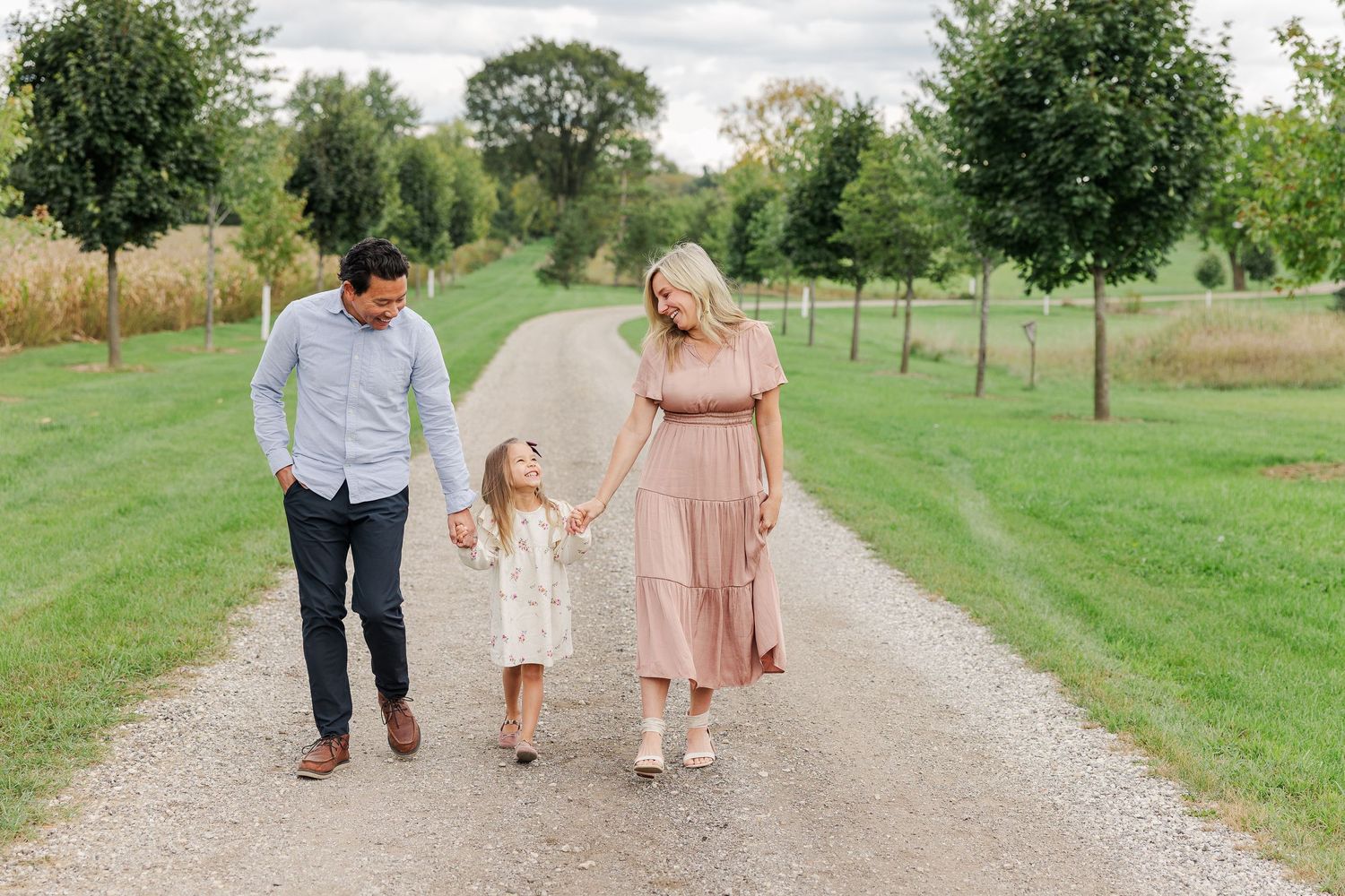 A family takes a stroll together on a tree-lined gravel path in summer.