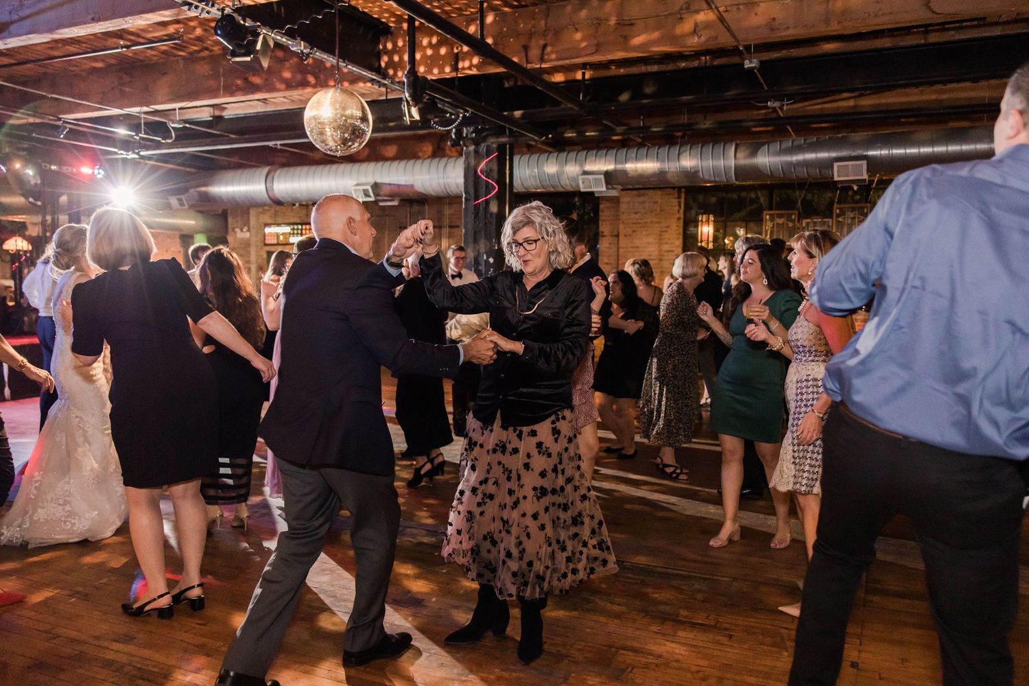 Wedding reception guests dancing in an industrial venue with exposed brick and ductwork.