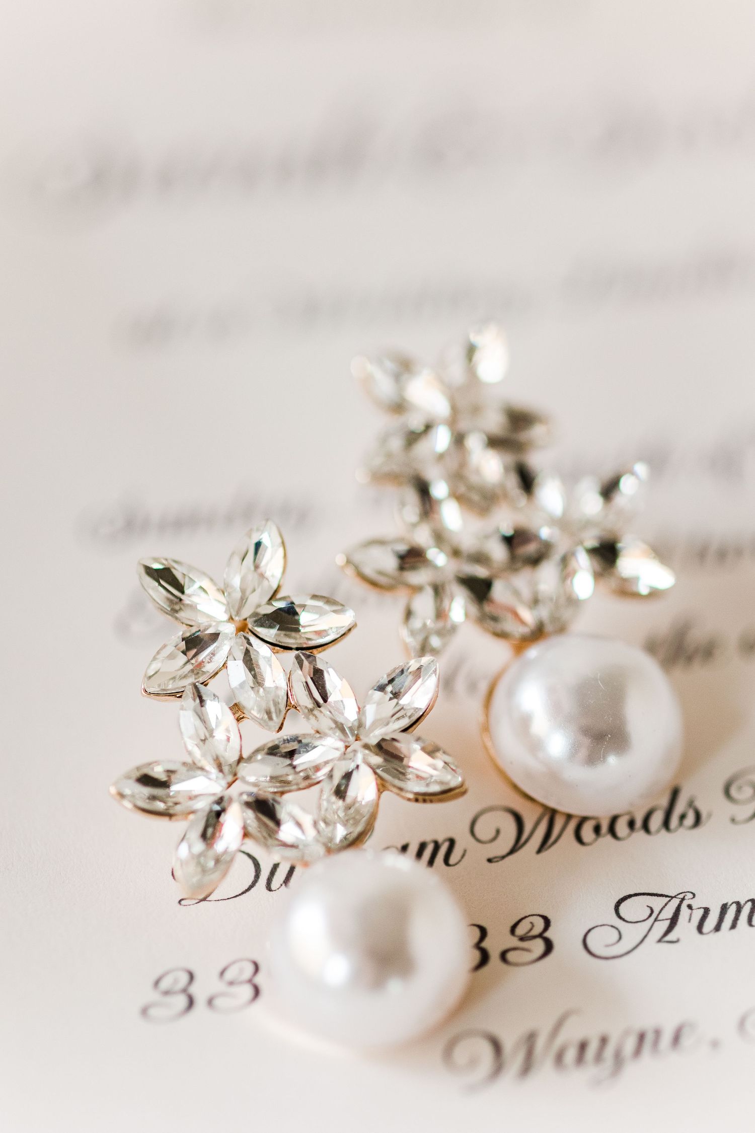 Crystal flower earrings and pearl accents displayed on a printed invitation.