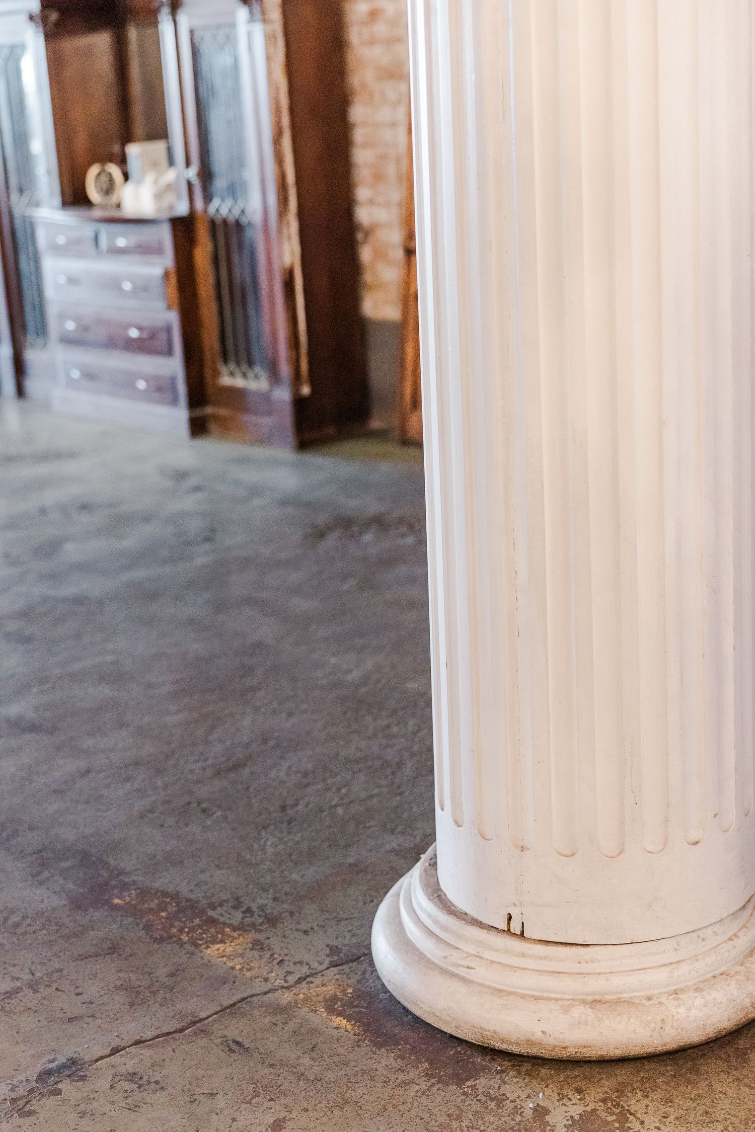 Close-up of a white fluted column base on concrete floor in an antique interior setting.