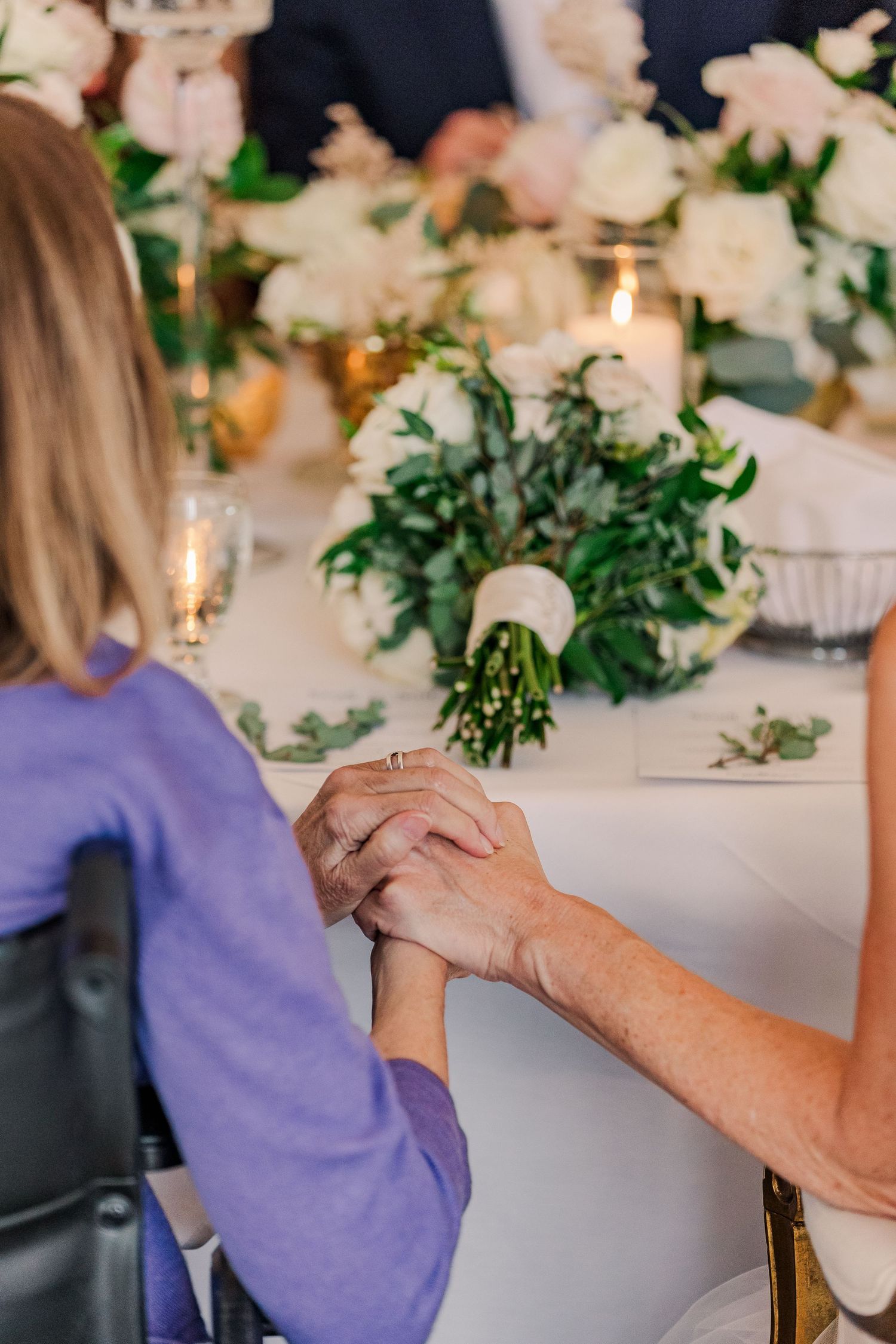 Intimate moment captured at wedding reception with hands clasped across elegant table setting.