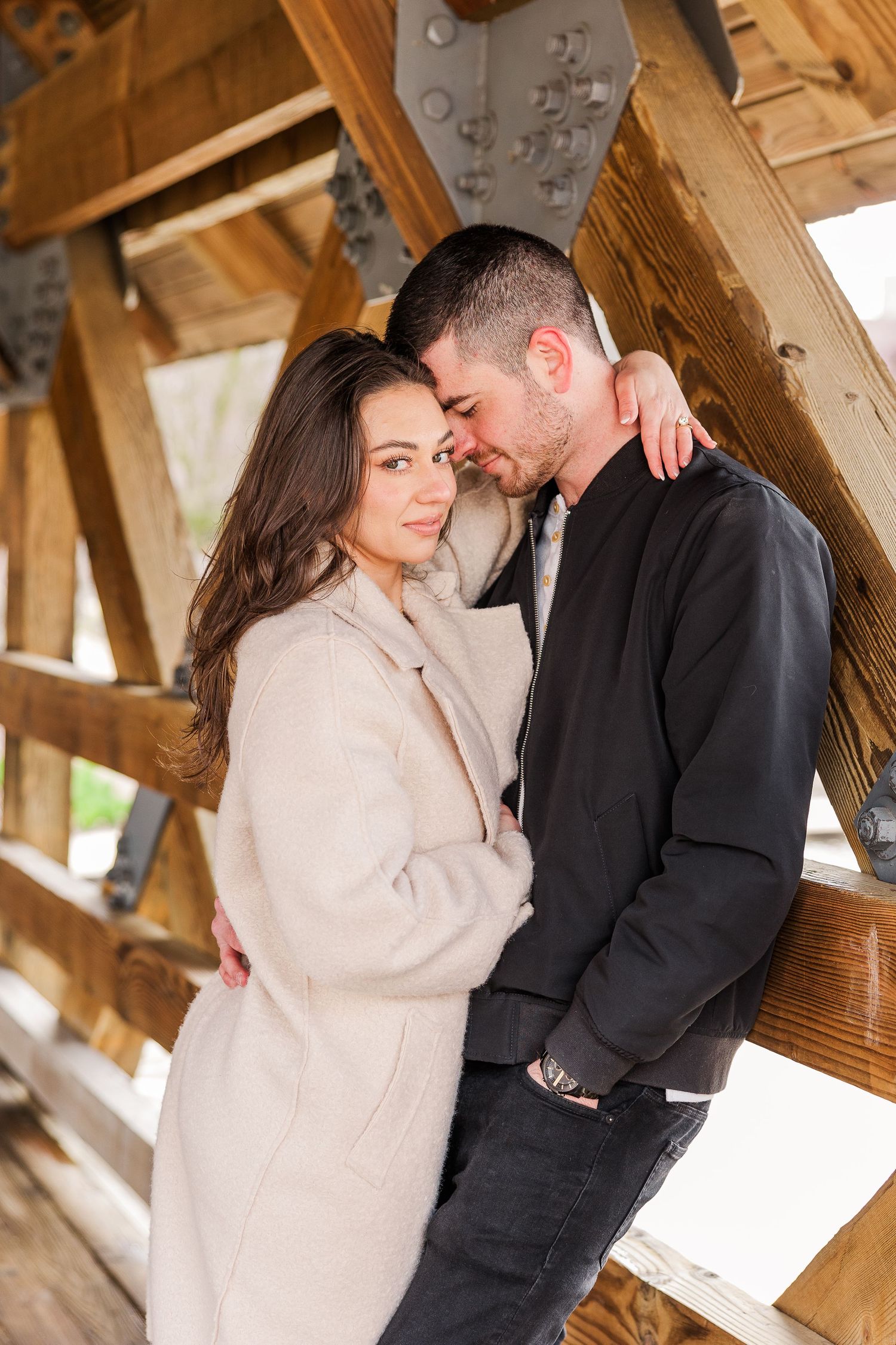 Intimate portrait of couple embracing under wooden beams in covered bridge.