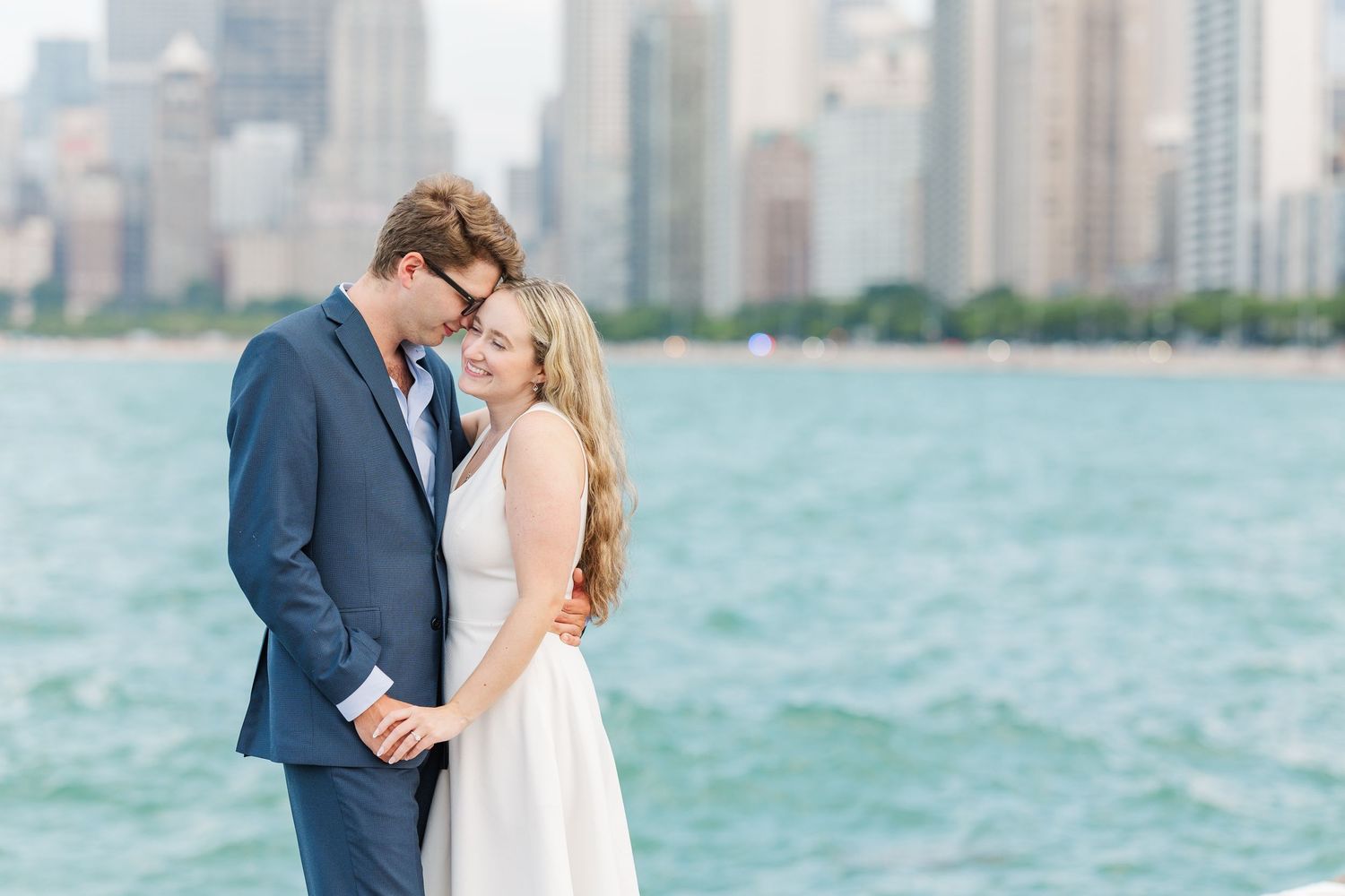 Elizabeth and Joe holding hands with the Chicago skyline in the background at North Avenue Beach during sunset