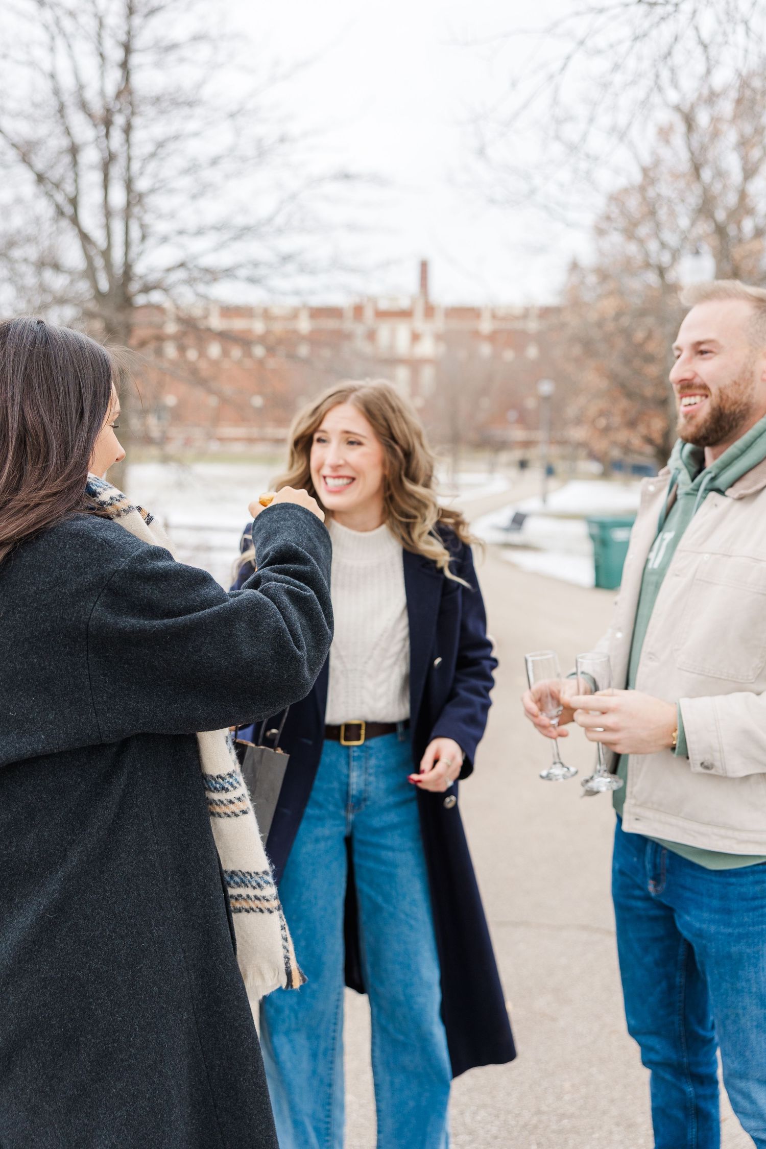 friend brings champagne and glasses to couple as to celebrate their engagement, Winnemac Park Chicago in Winter