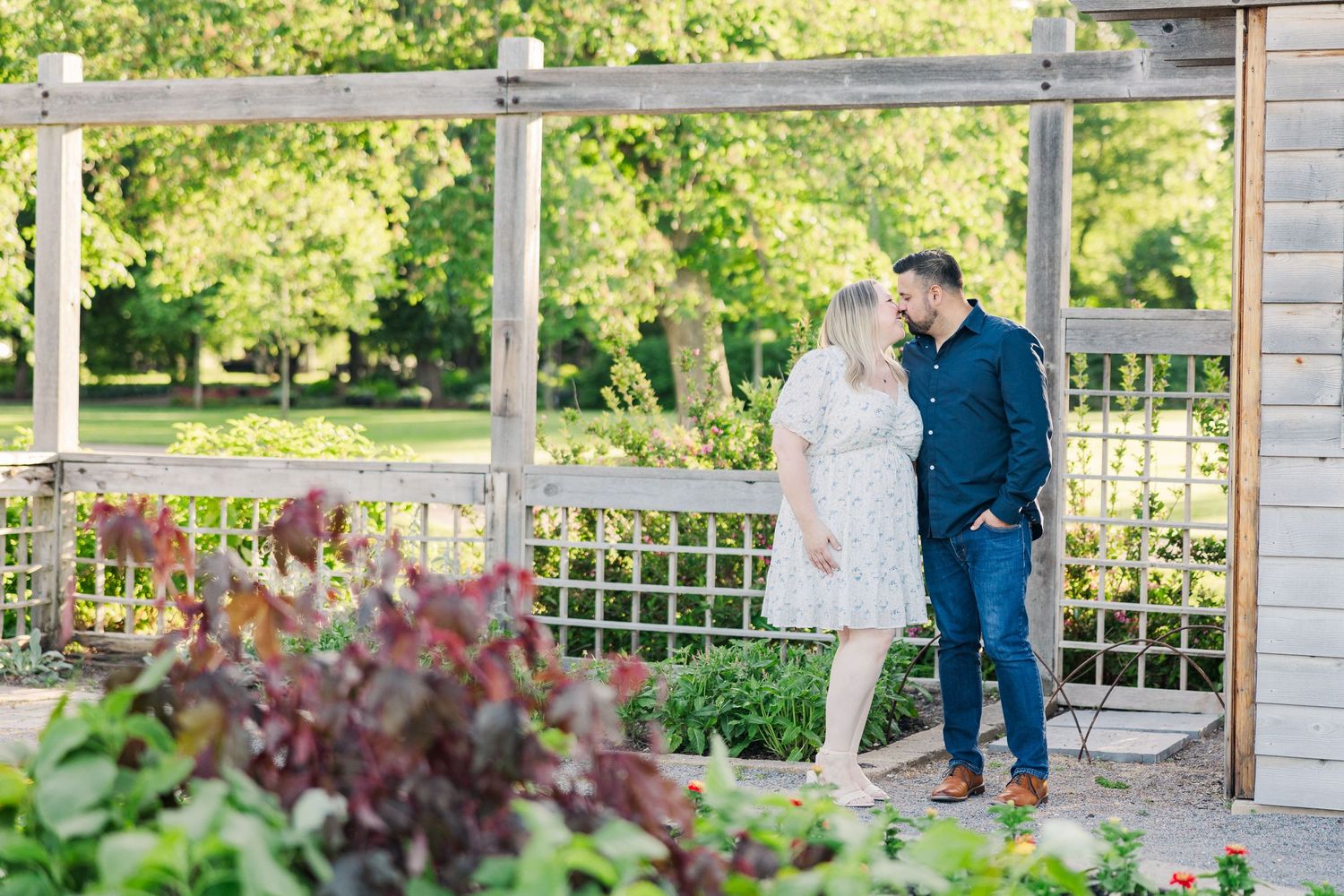 A couple shares an intimate moment on a garden pergola surrounded by lush landscaping.