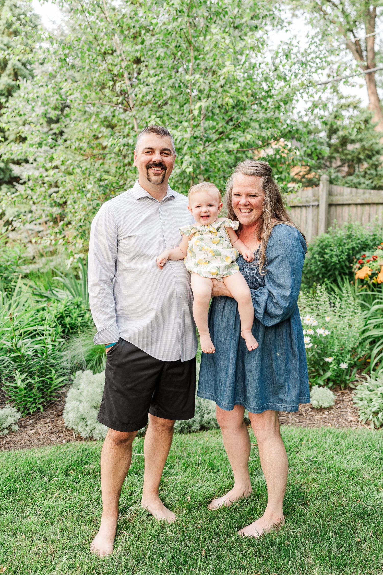 Barefoot family portrait in a backyard garden with blooming flowers and greenery.