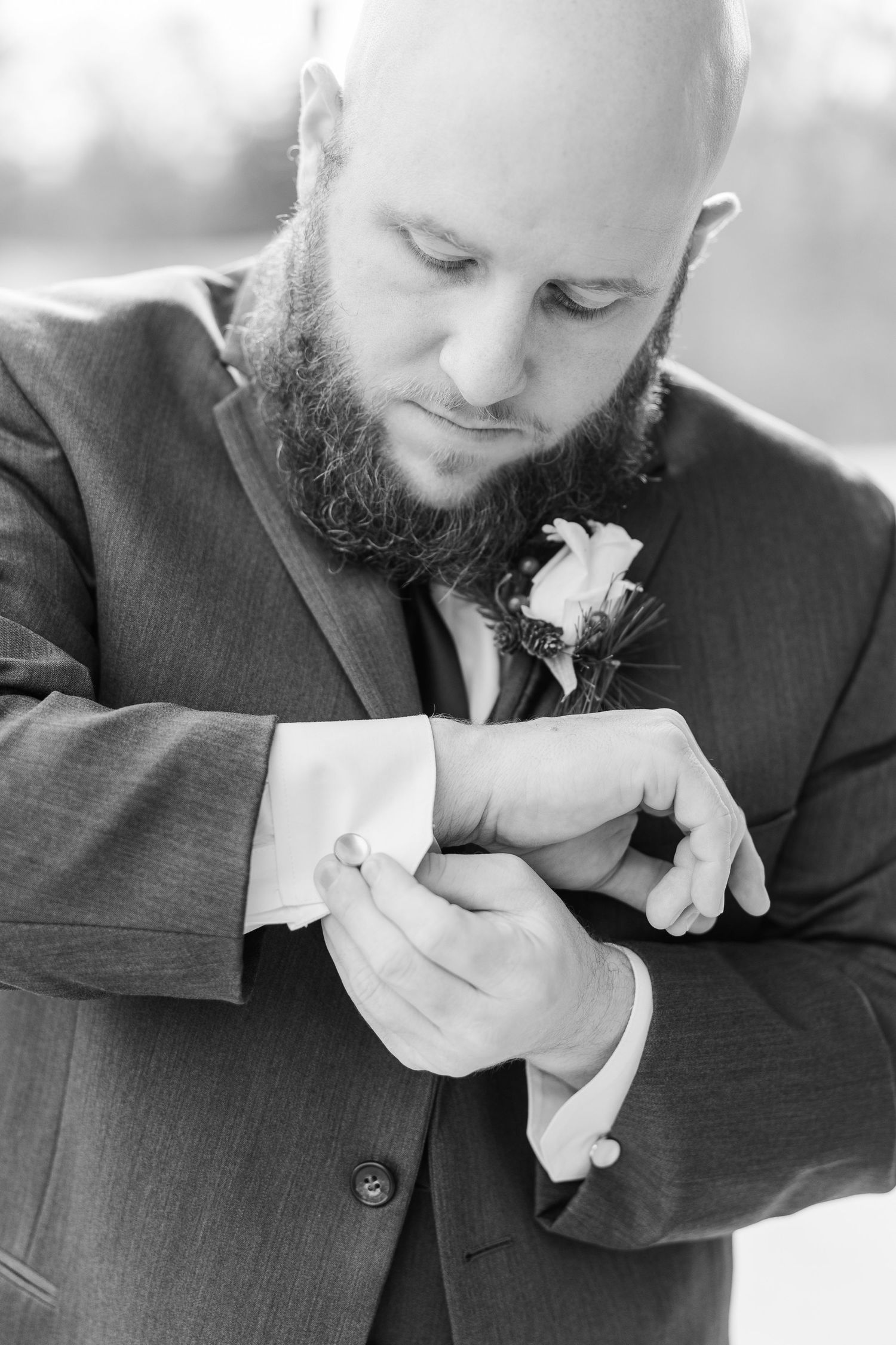 Person in dark suit adjusting boutonniere in black and white photo.